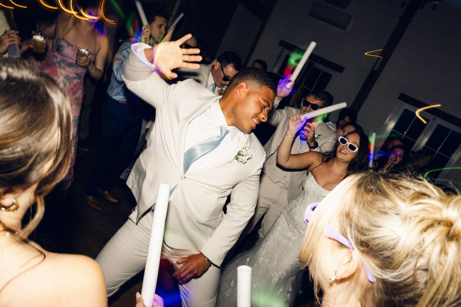 Energetic wedding reception dance floor with guests dancing under colorful glow stick lights.