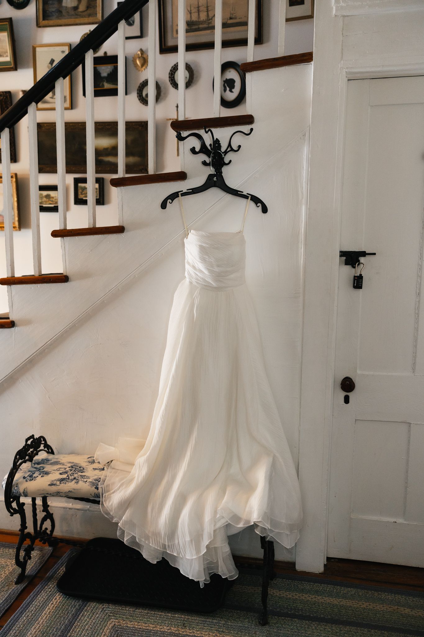 Elegant white strapless wedding gown displayed on a decorative black hanger near a staircase.