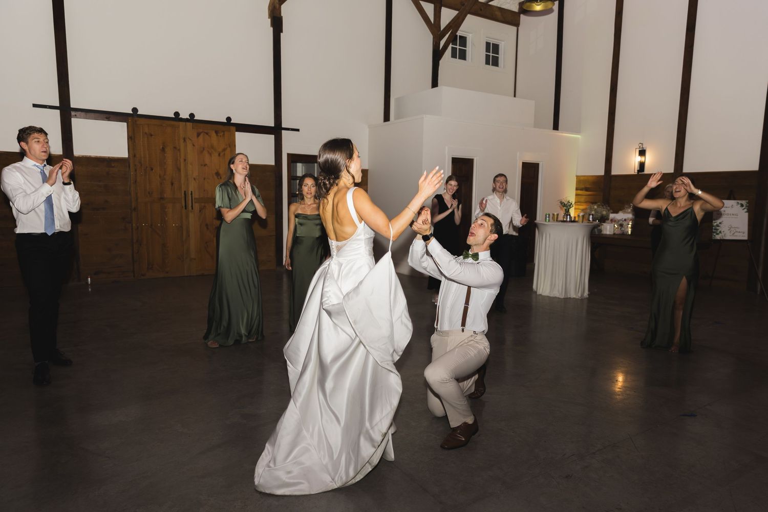 Bride and groom perform a dramatic dance lift in a barn reception hall surrounded by cheering guests.