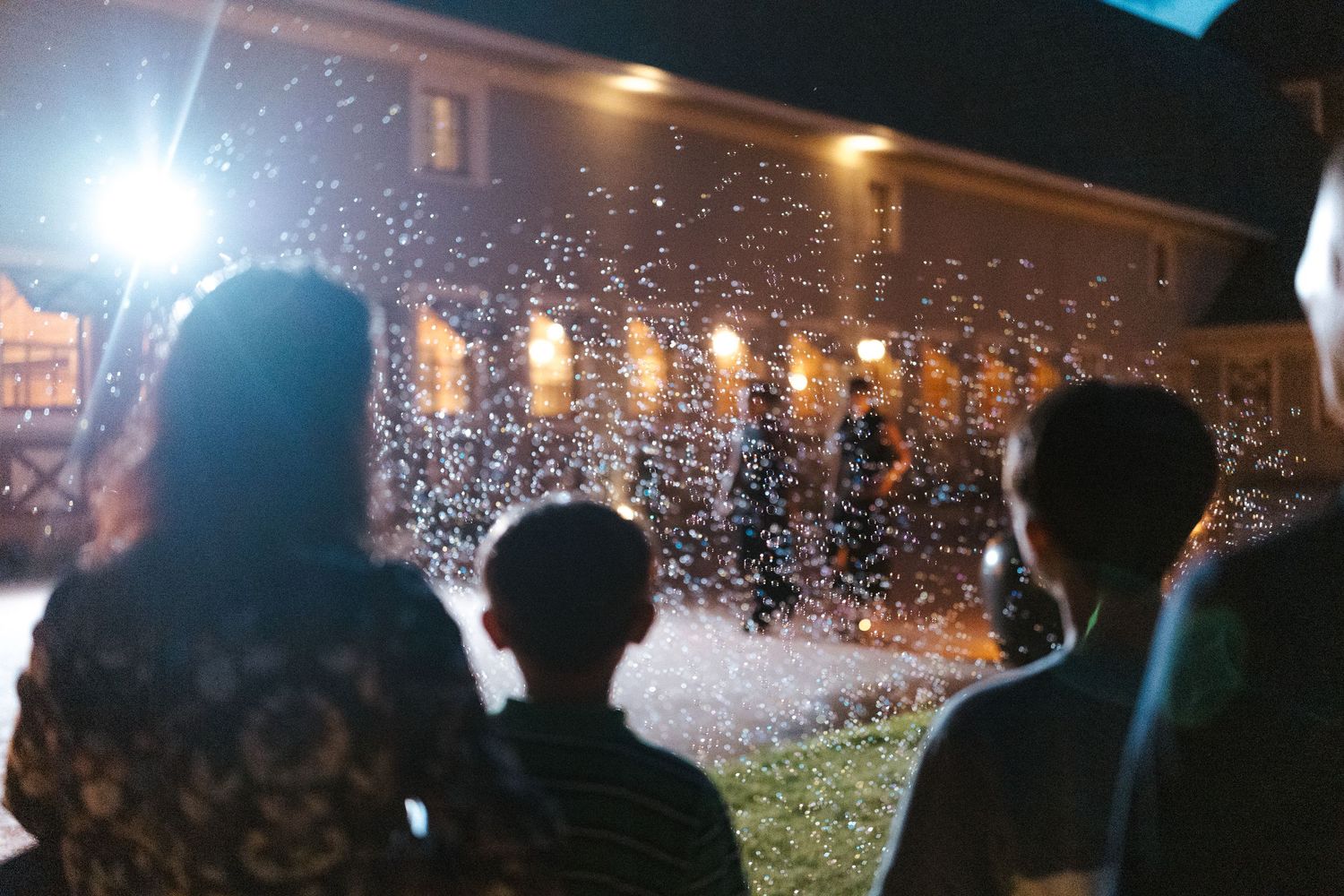 Family watching a festive confetti celebration outdoors at night near an illuminated building.