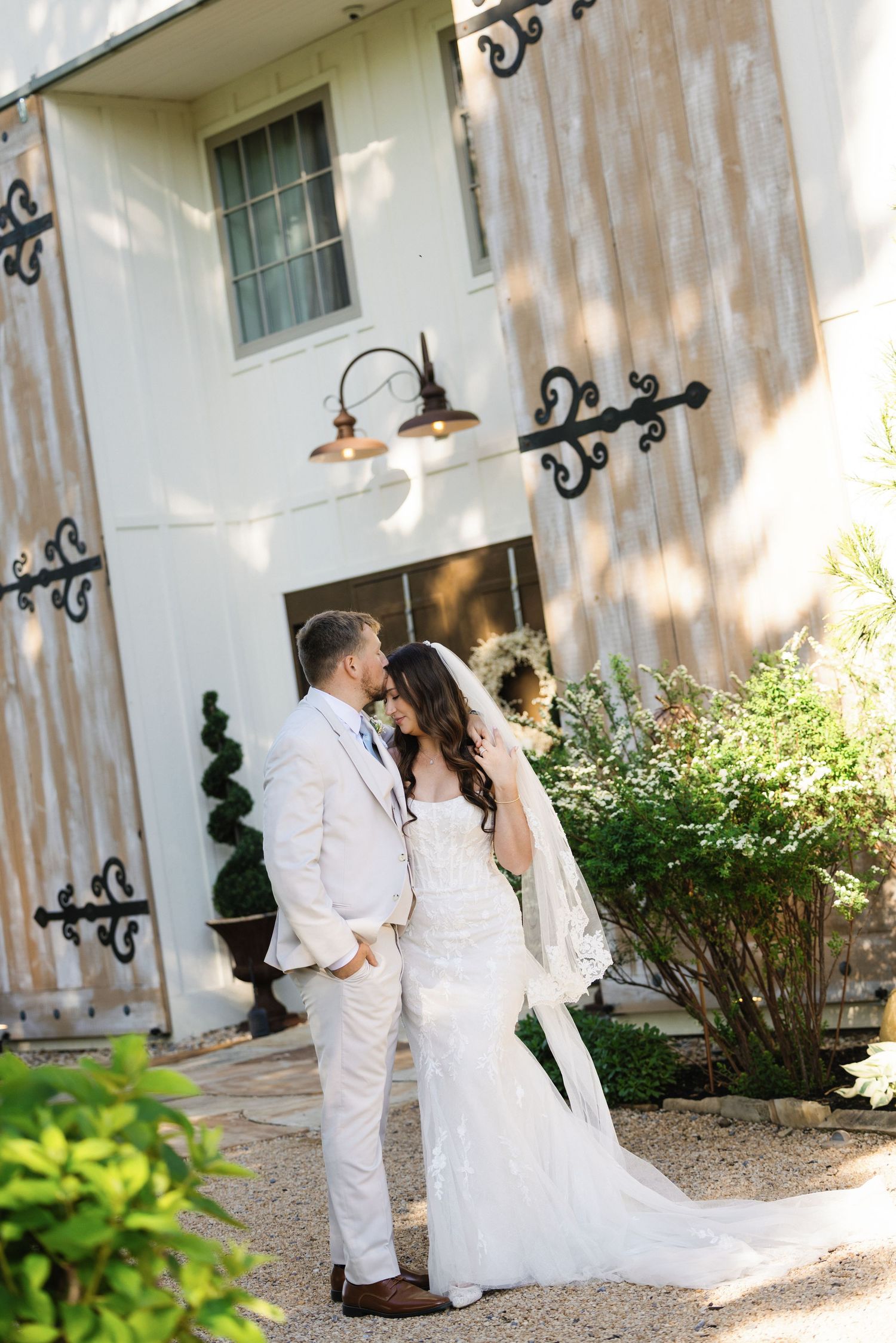 Bride and groom share a romantic moment outside a rustic white barn wedding venue.