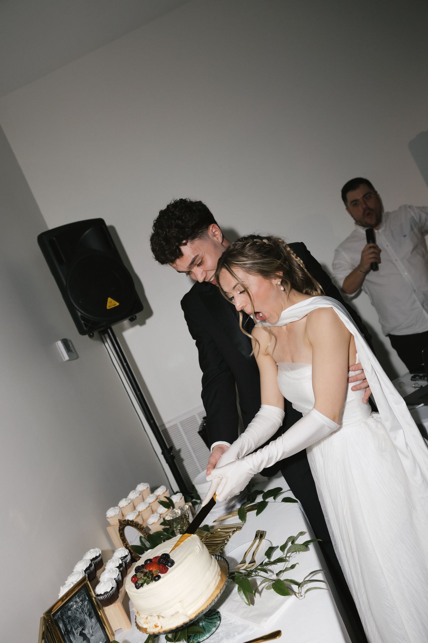 Bride and groom laughing while cutting their white wedding cake at their reception.