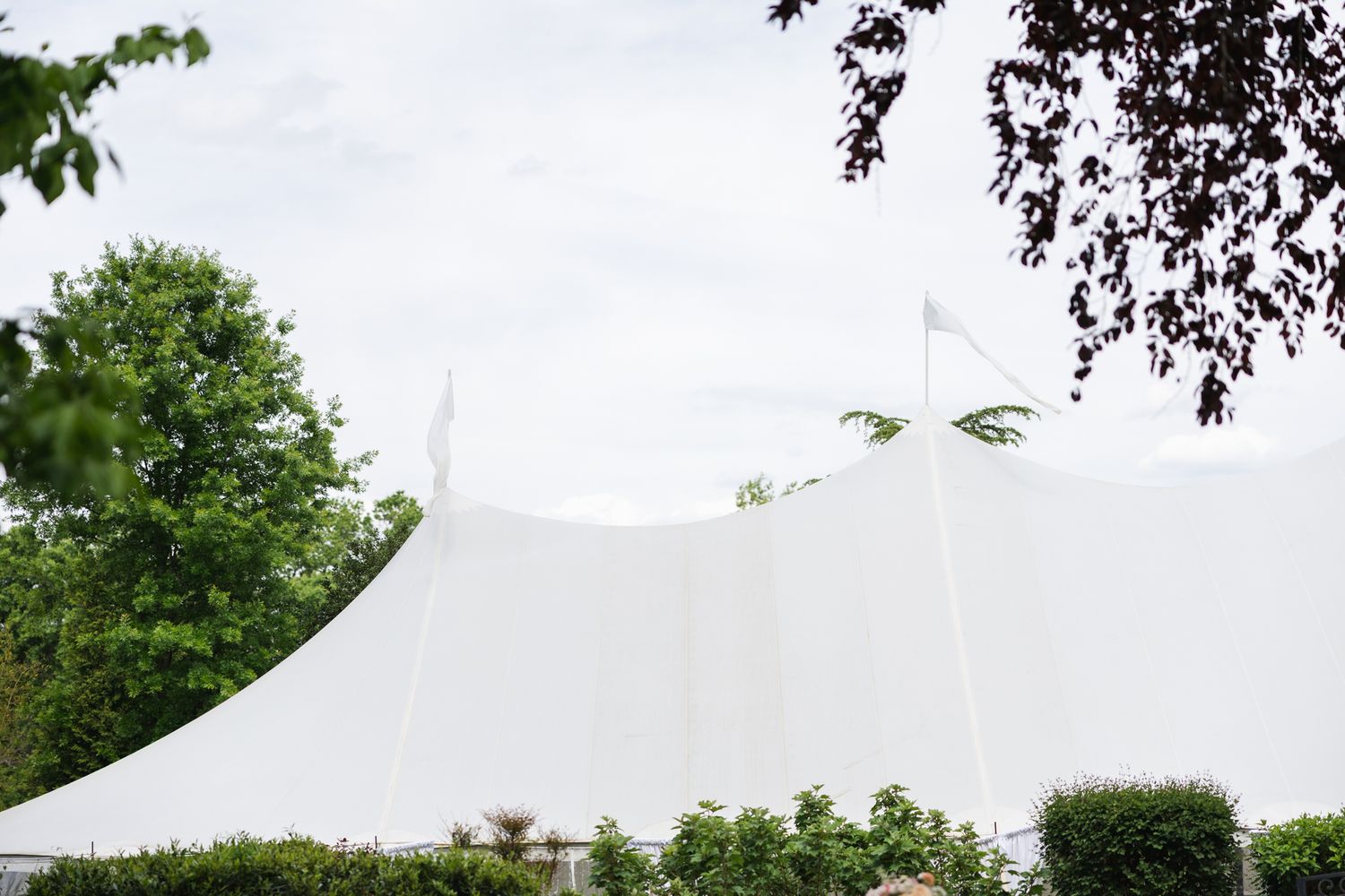 Large white wedding tent surrounded by lush green trees against a cloudy sky.