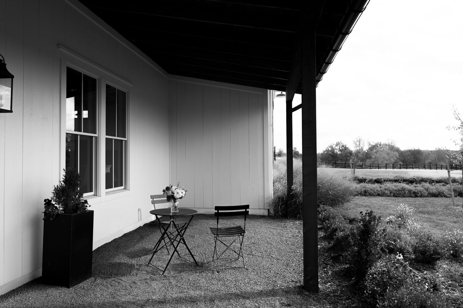 Black and white photo of a quiet barn venue porch with bistro chairs and open countryside views.