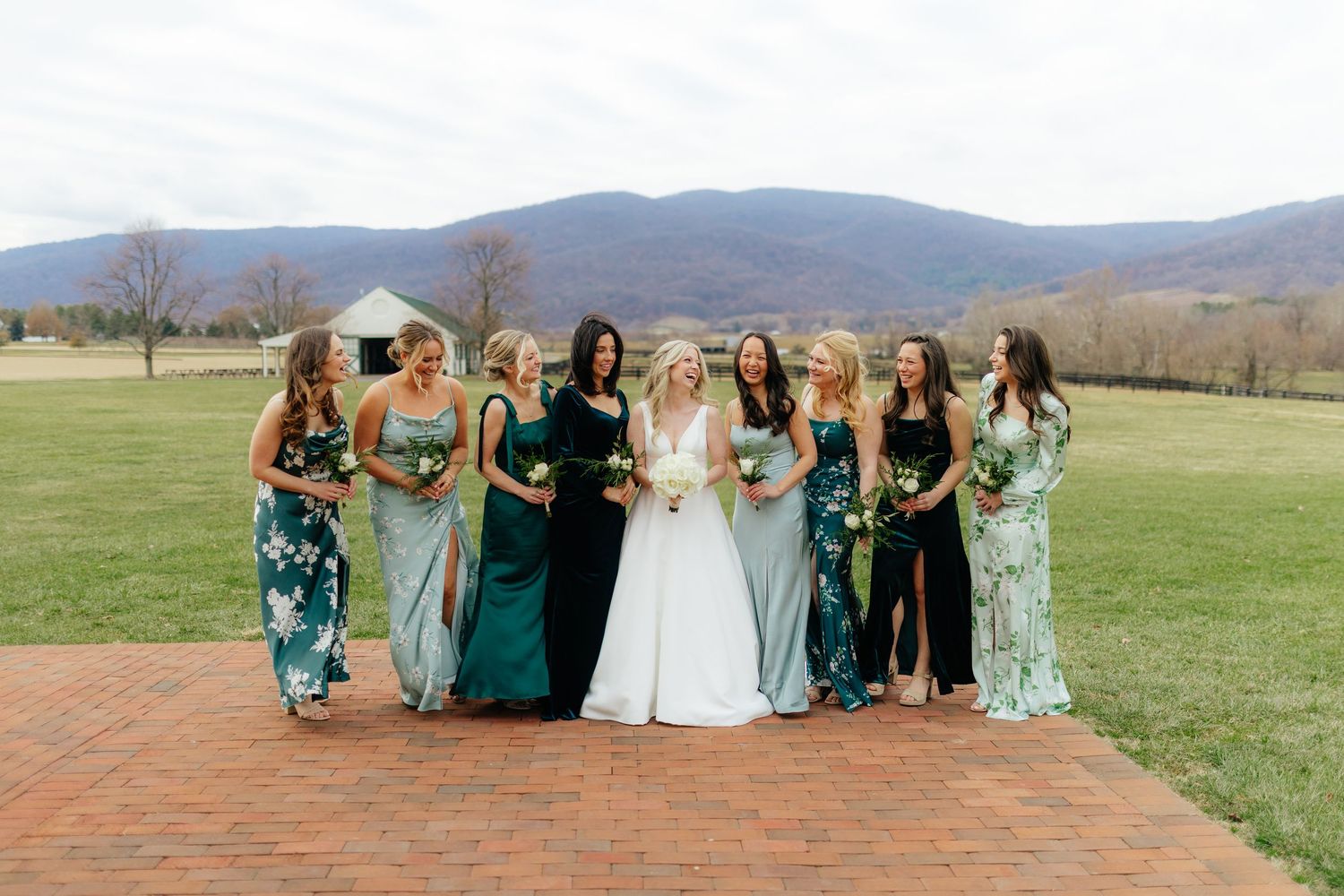 Bride in white gown poses with nine bridesmaids in green dresses against a mountain backdrop.