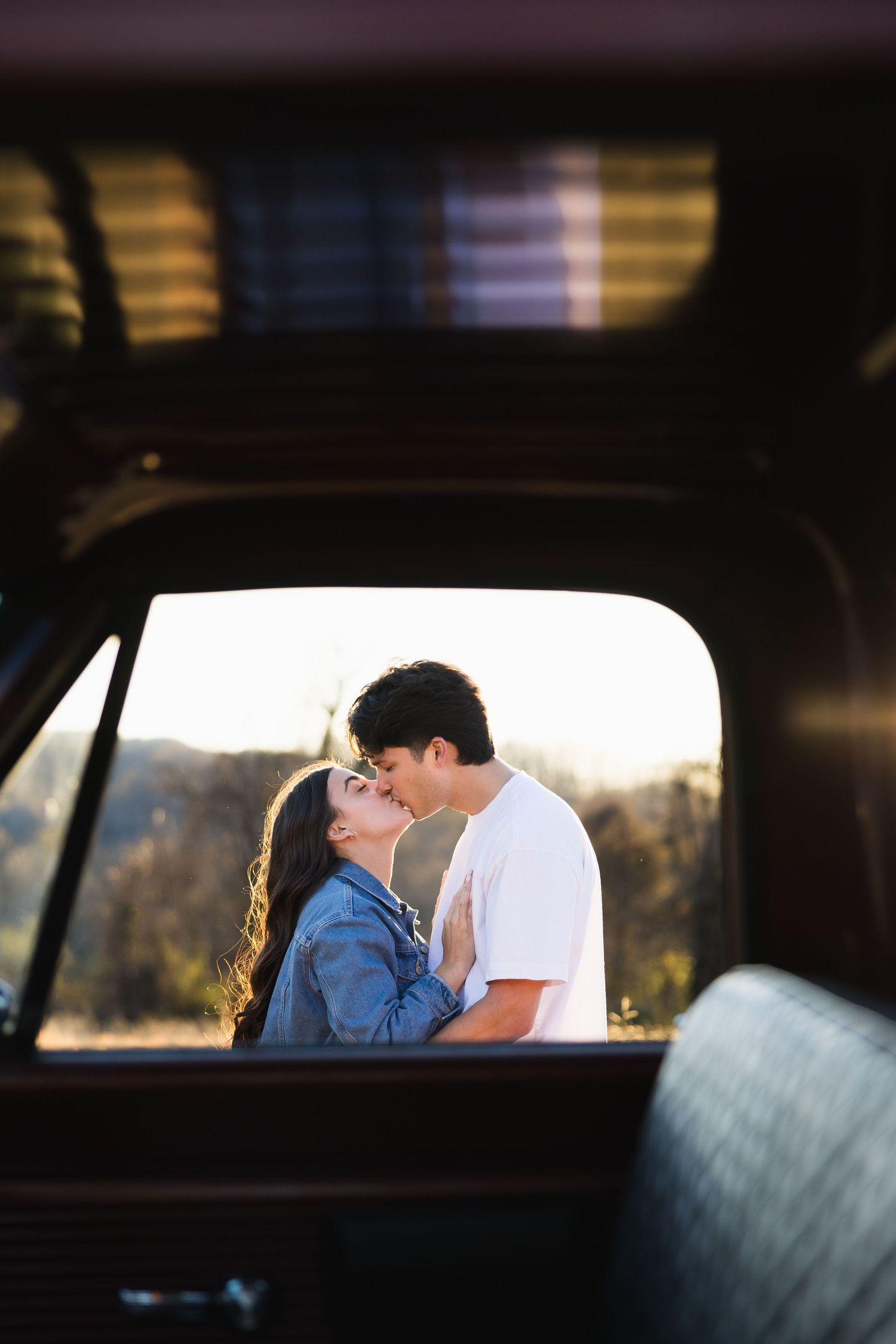 Romantic couple about to kiss framed through the window of a vintage truck with warm sunset light behind them.