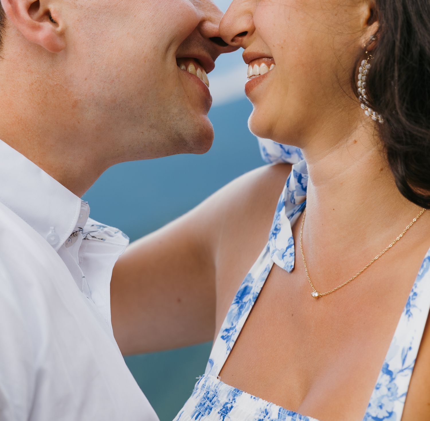 Smiling couple nose to nose about to kiss outdoors near water.