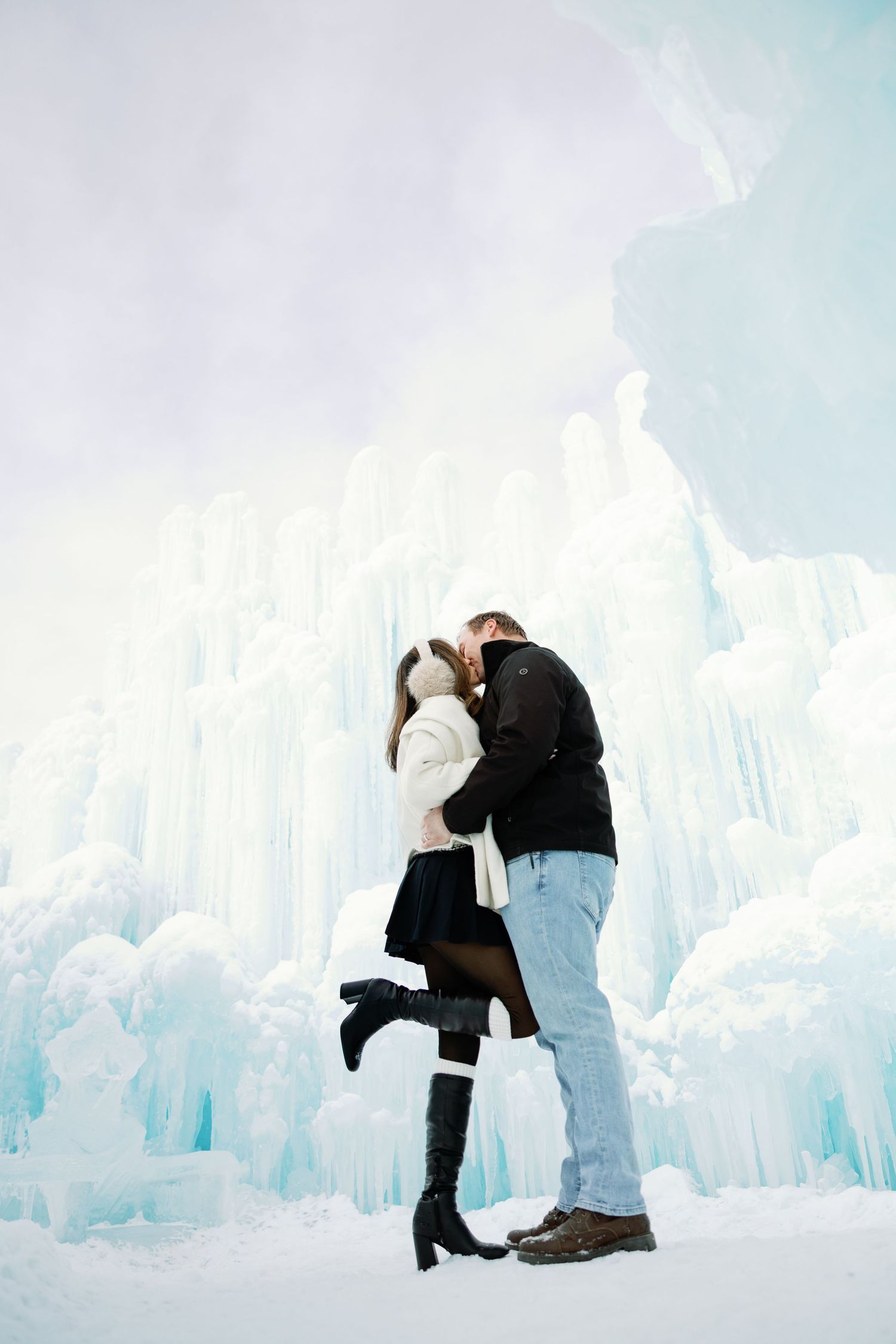 Couple shares a sweet kiss while posing in front of breathtaking blue ice castle formations.