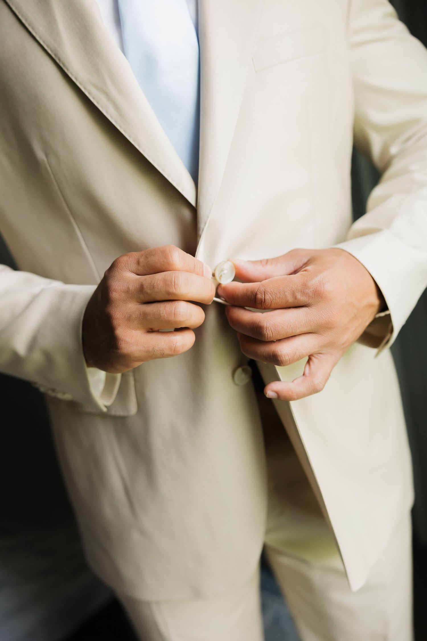 Man in beige suit buttoning jacket, elegant formal attire for wedding or special occasion.