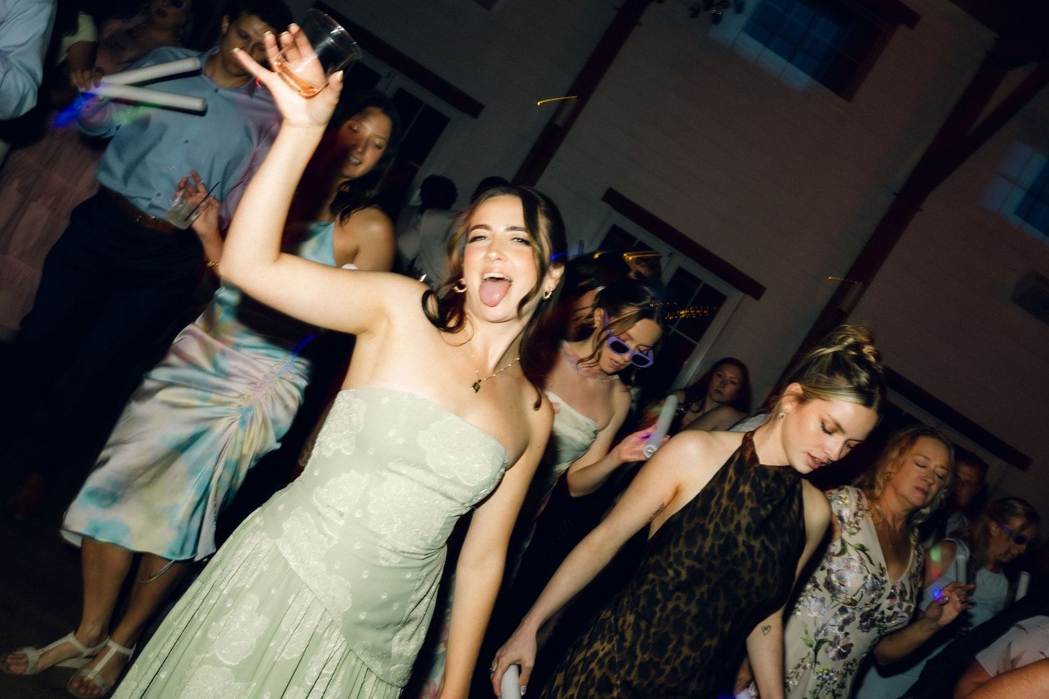 Bridesmaid in sage green dress dances energetically at lively wedding reception celebration.