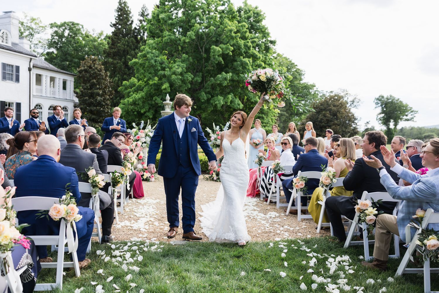 Happy newlyweds walk back down the aisle as bride raises bouquet in celebration outdoors.
