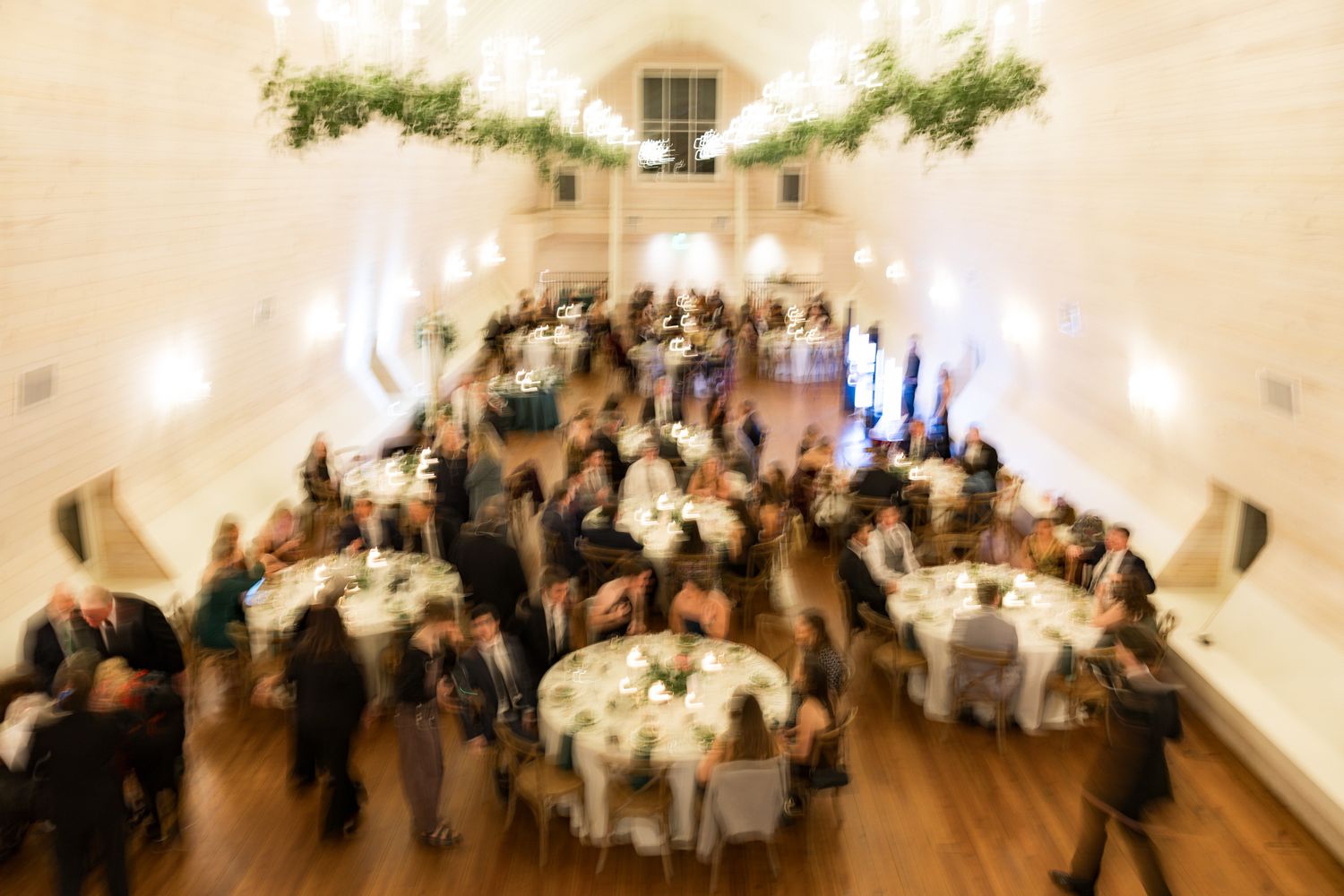 Aerial view of elegant wedding reception in vaulted hall with round tables.