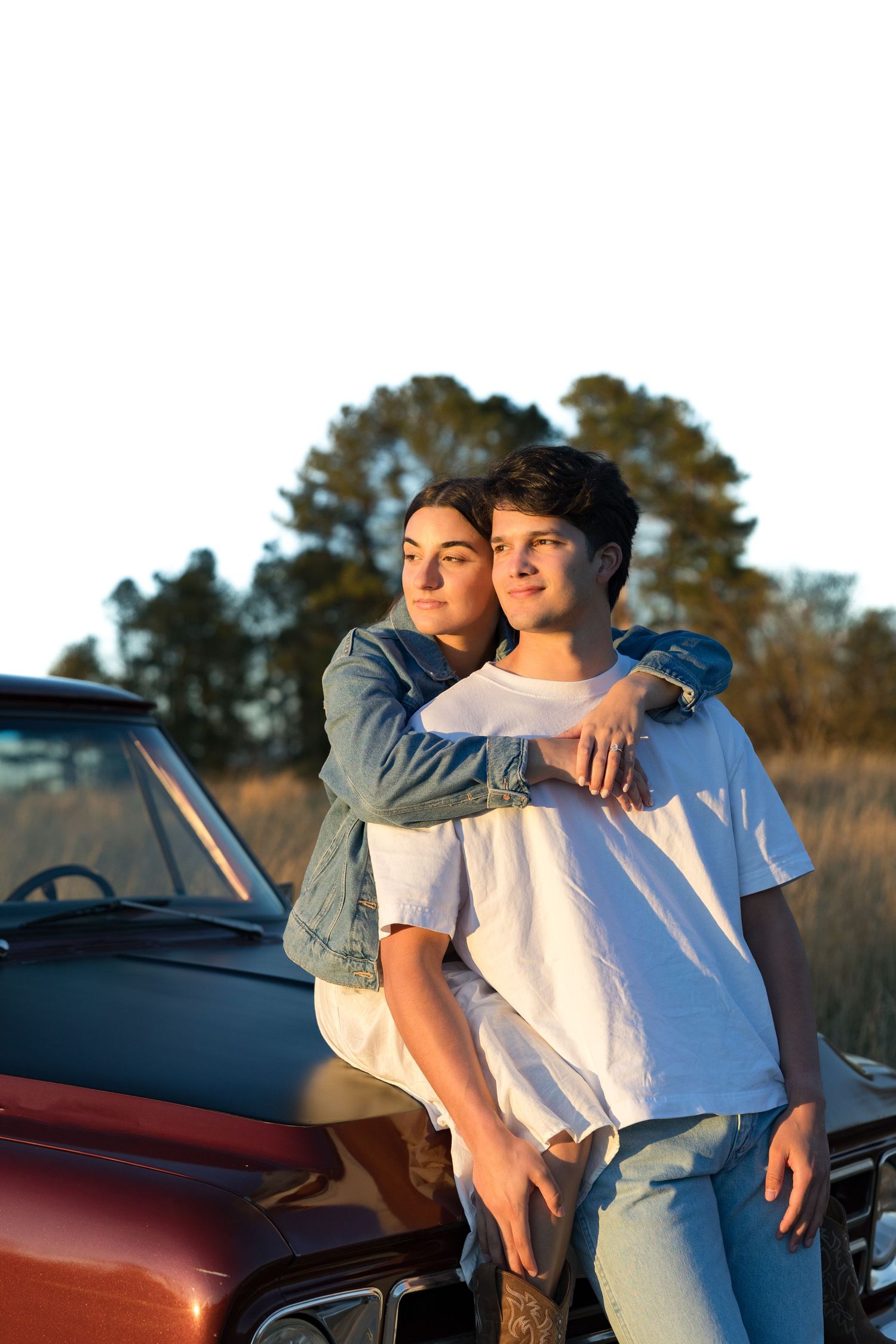A couple leaning against a red vintage truck at golden hour, the woman embracing the man from behind.