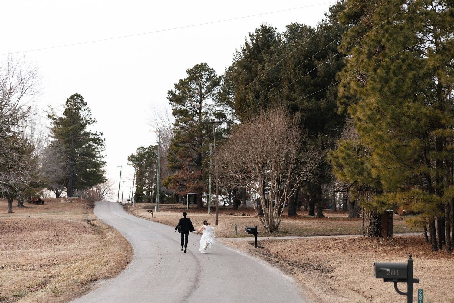 Bride and groom walk together down a winding road surrounded by winter trees after their wedding.