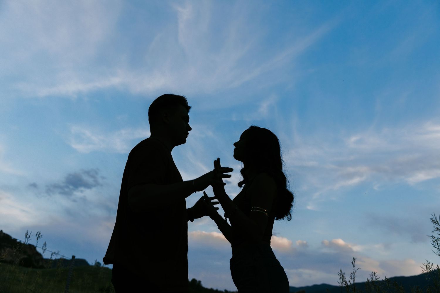Silhouette of couple sharing a romantic moment against a vibrant blue twilight sky at dusk outdoors.