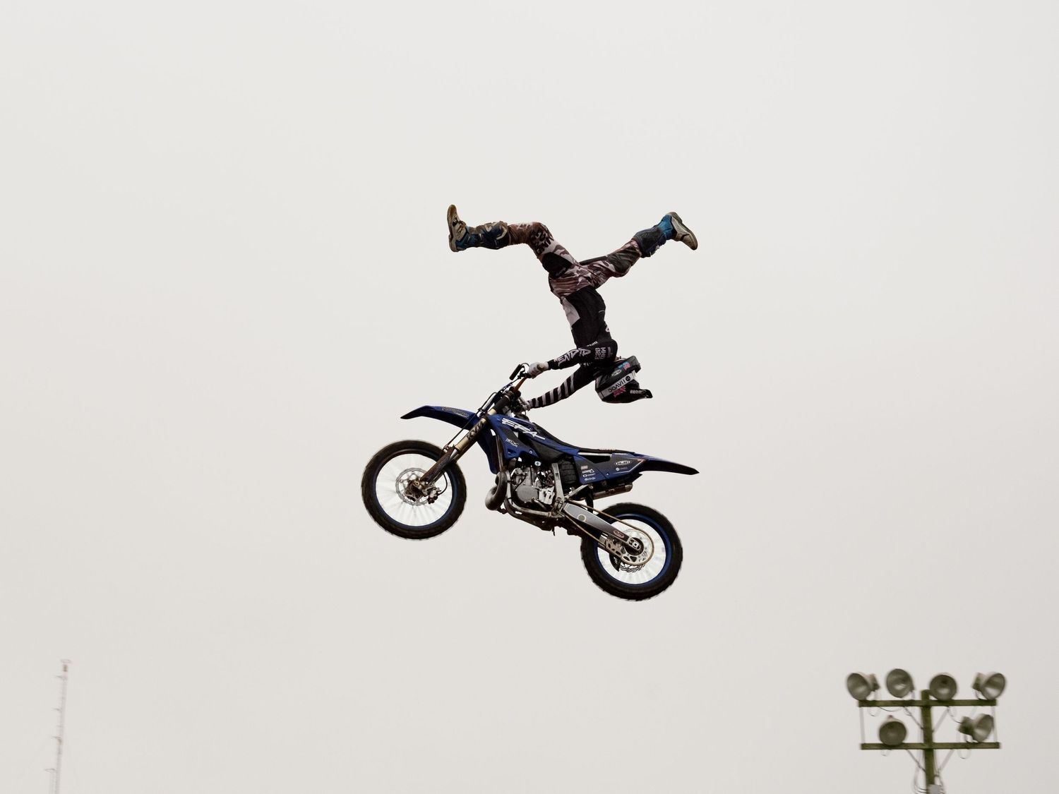 Silhouette of a motocross rider performing an inverted aerial stunt against a light sky.
