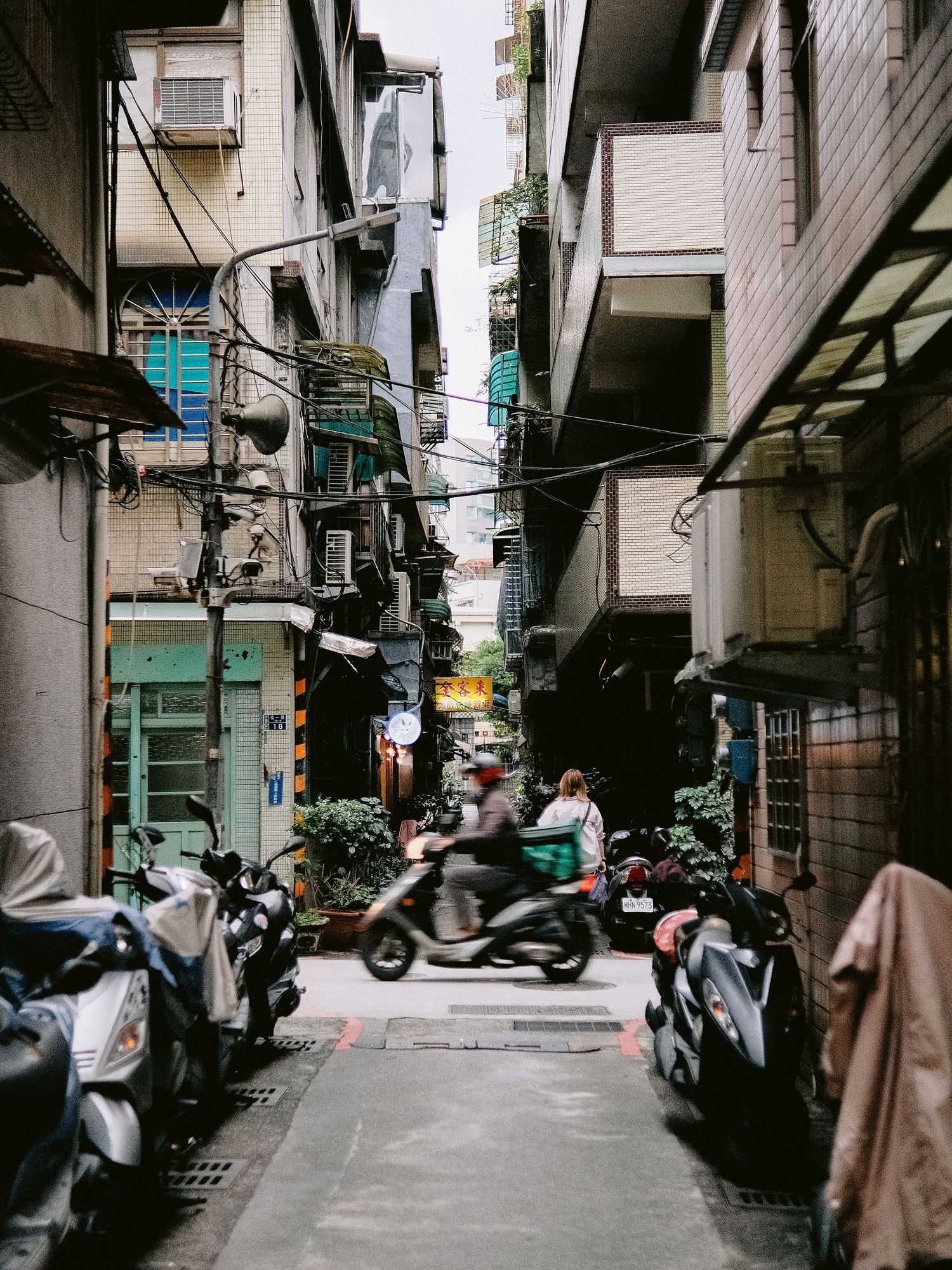 Narrow urban alley with parked motorcycles and apartment buildings in Asia.