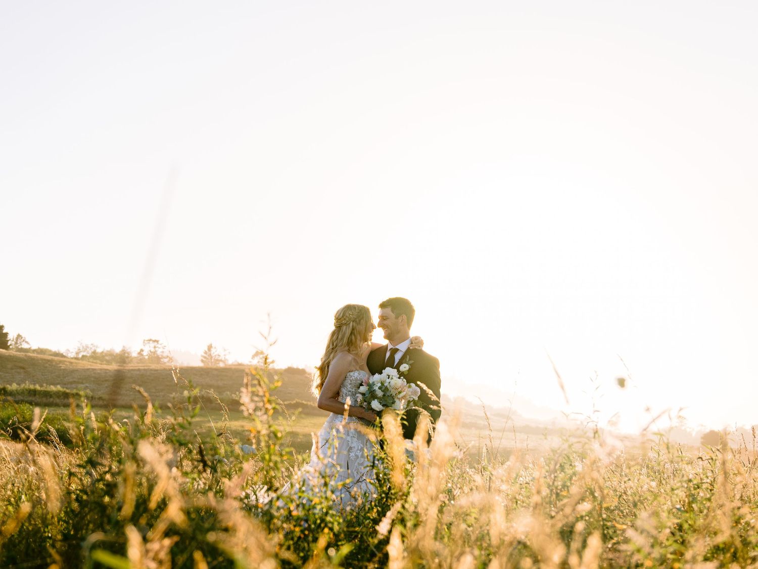 A romantic couple embraces in a sunlit meadow during golden hour creating a dreamy silhouette against the setting sun.