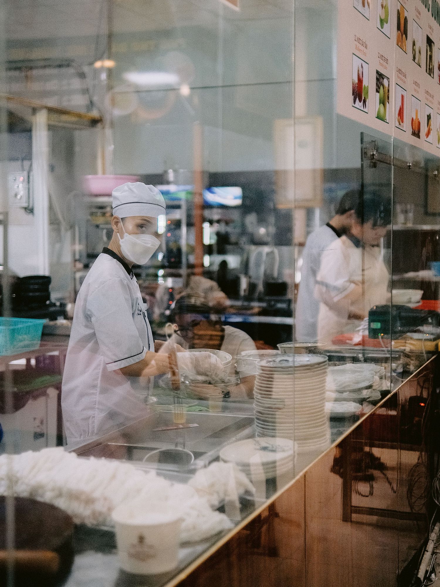 Kitchen staff working behind glass counter in a busy restaurant kitchen.