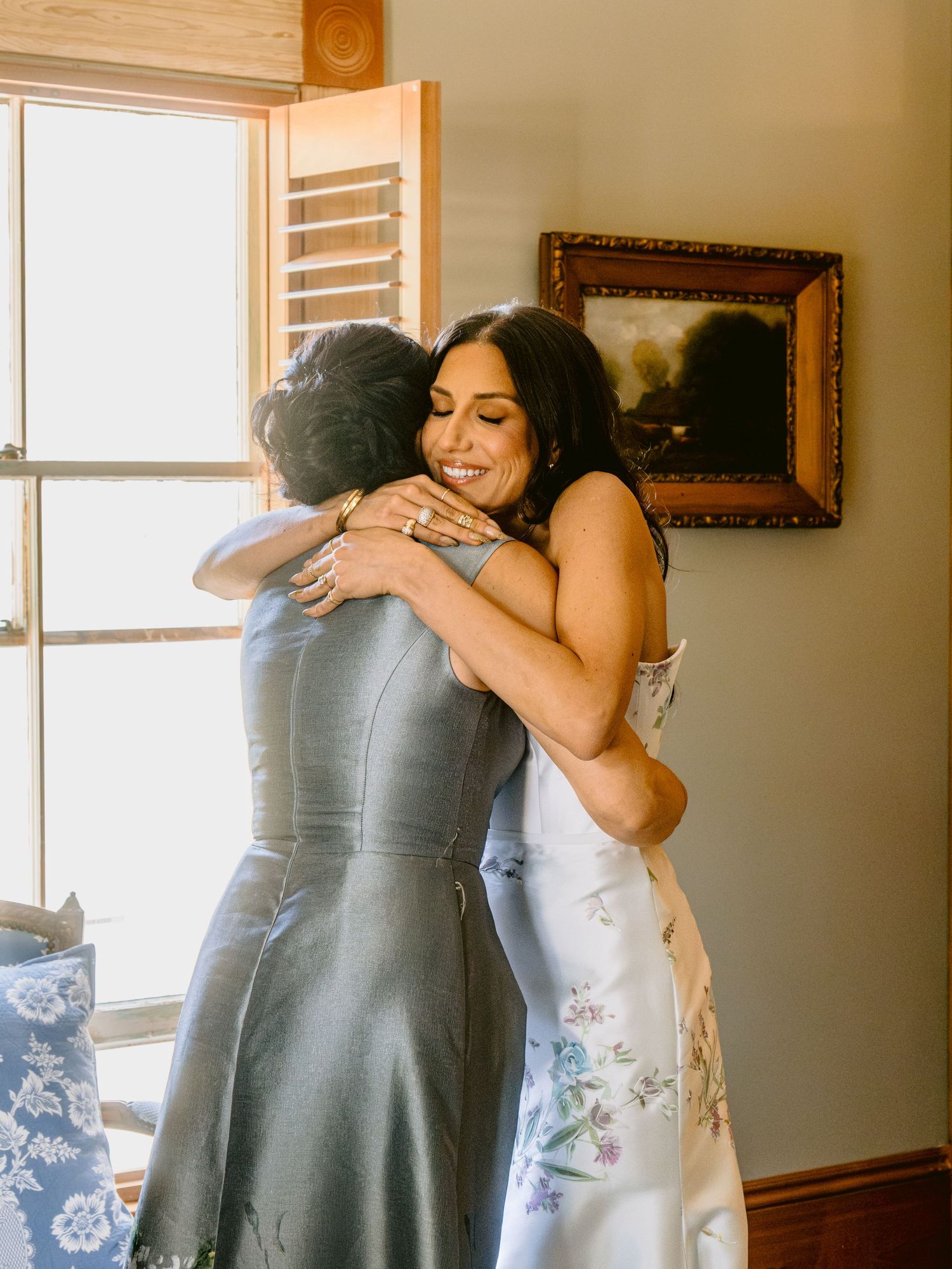 Emotional moments shared between wedding party members wearing grey dresses in sunlit room.