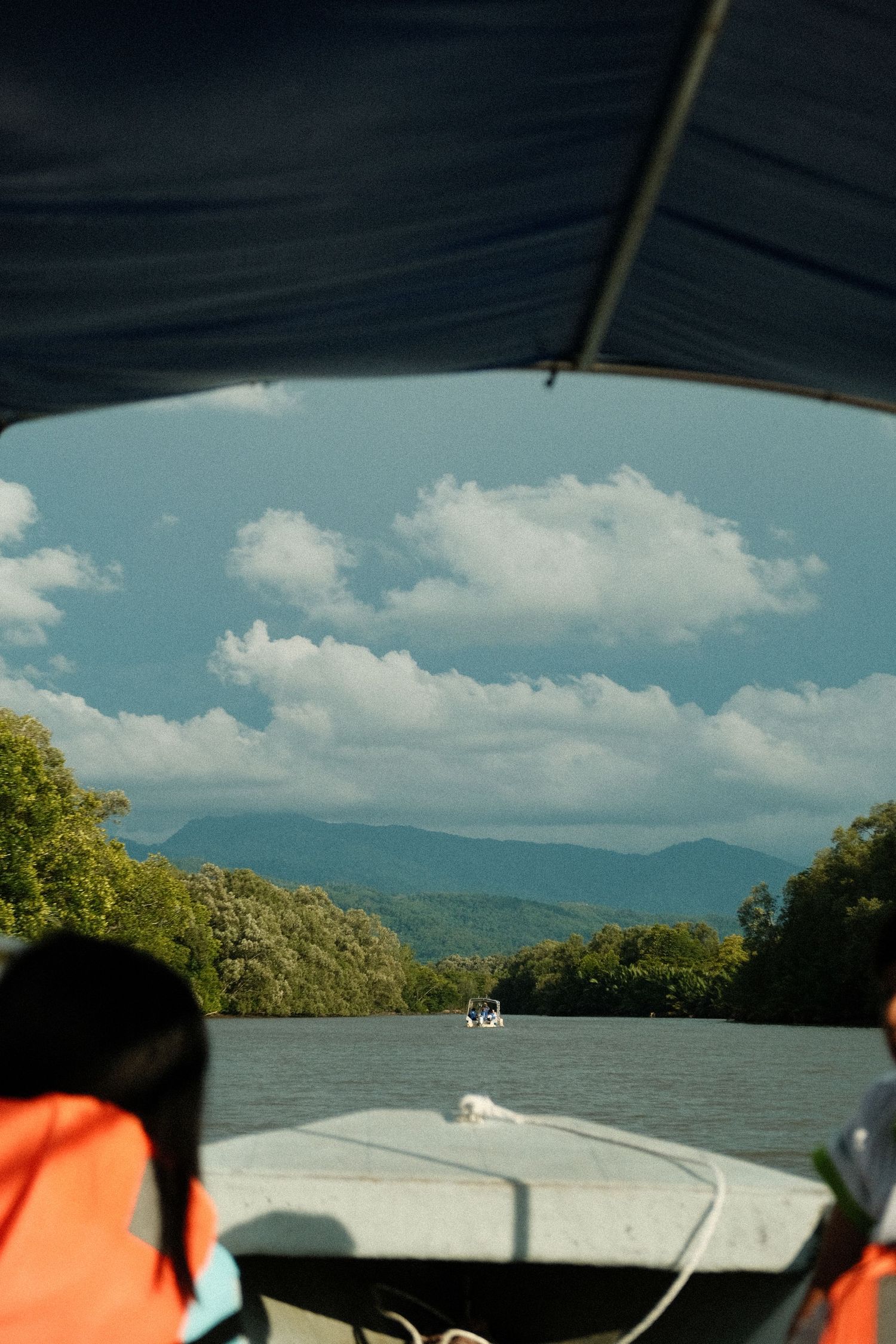 View of mountains and lake from boat with blue sky and white clouds overhead.