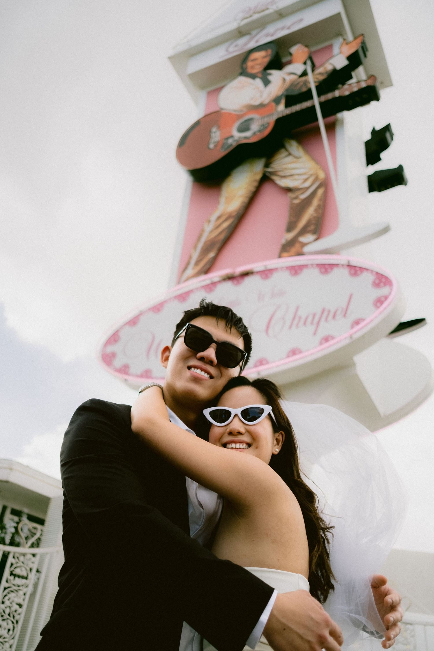 Playful wedding couple wearing sunglasses pose together outside a white chapel in Las Vegas.