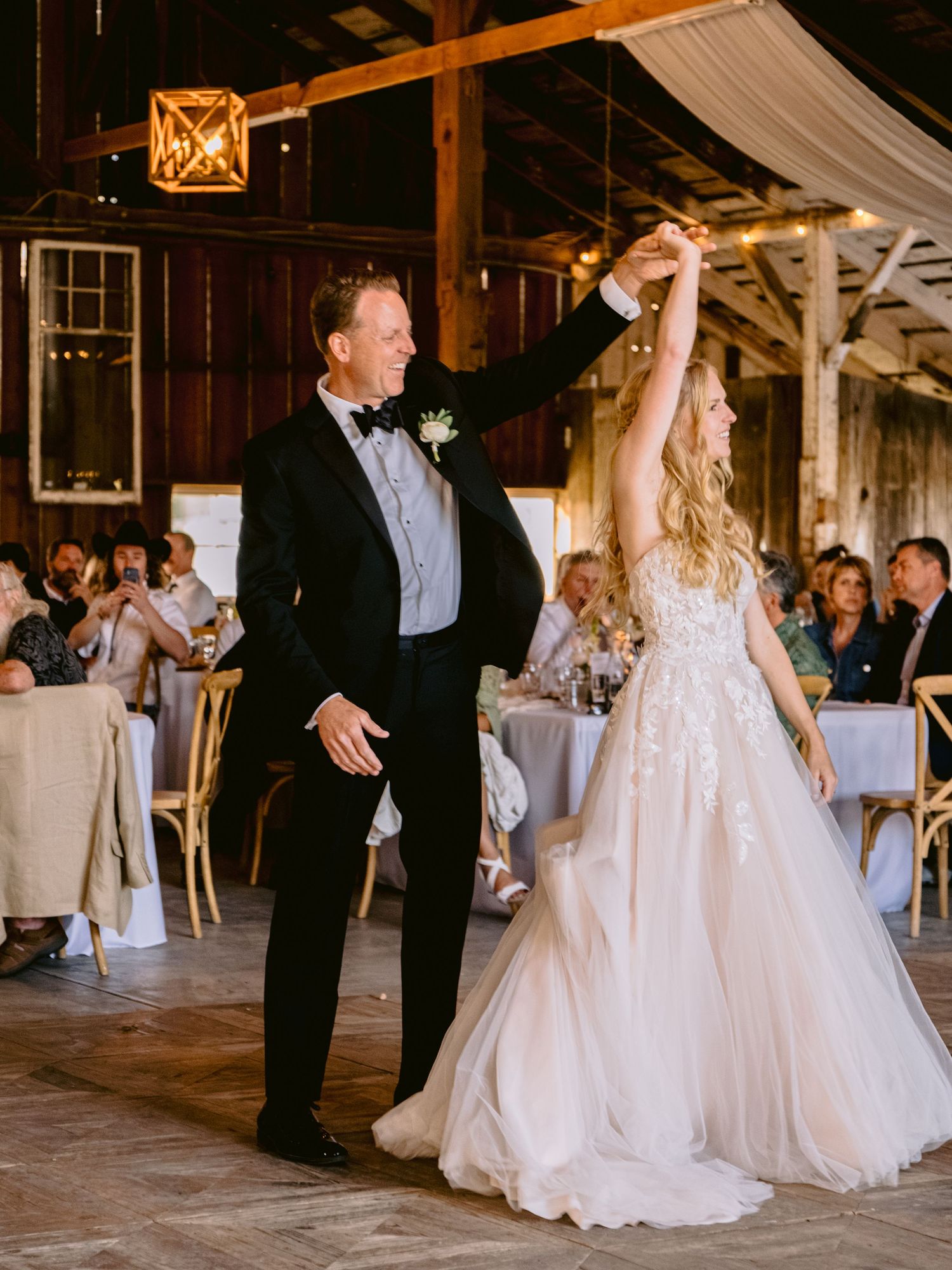 Wedding reception dance moments captured inside a rustic barn venue with draped fabric decor.