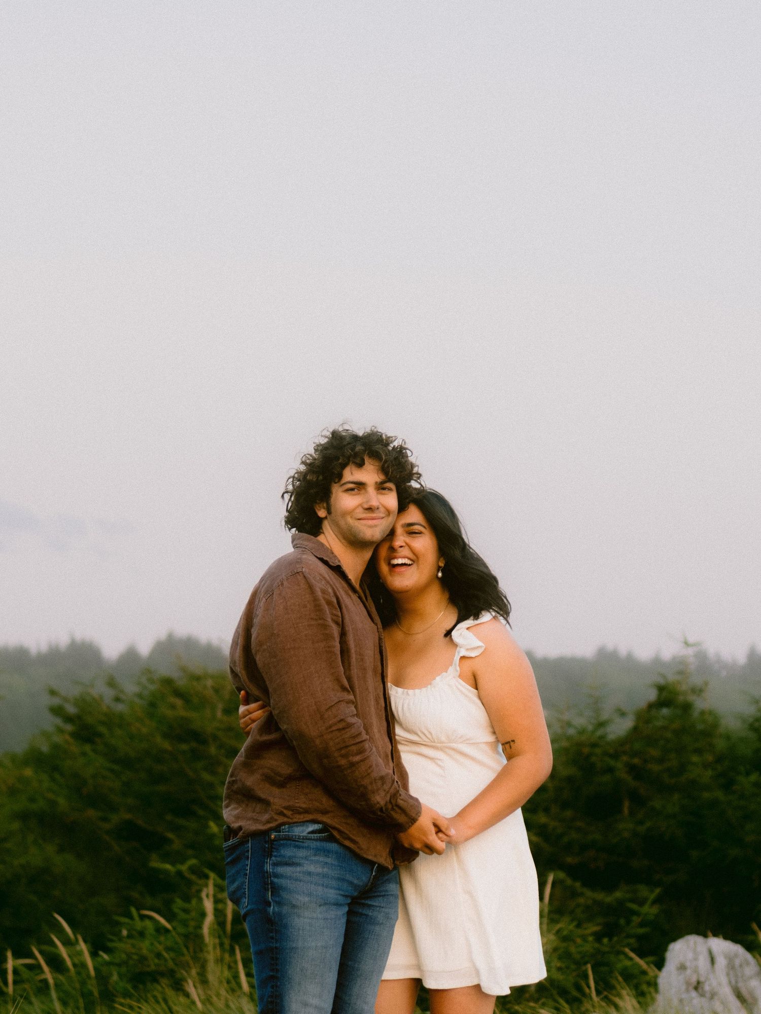 A couple shares an affectionate moment against a backdrop of evergreen trees.