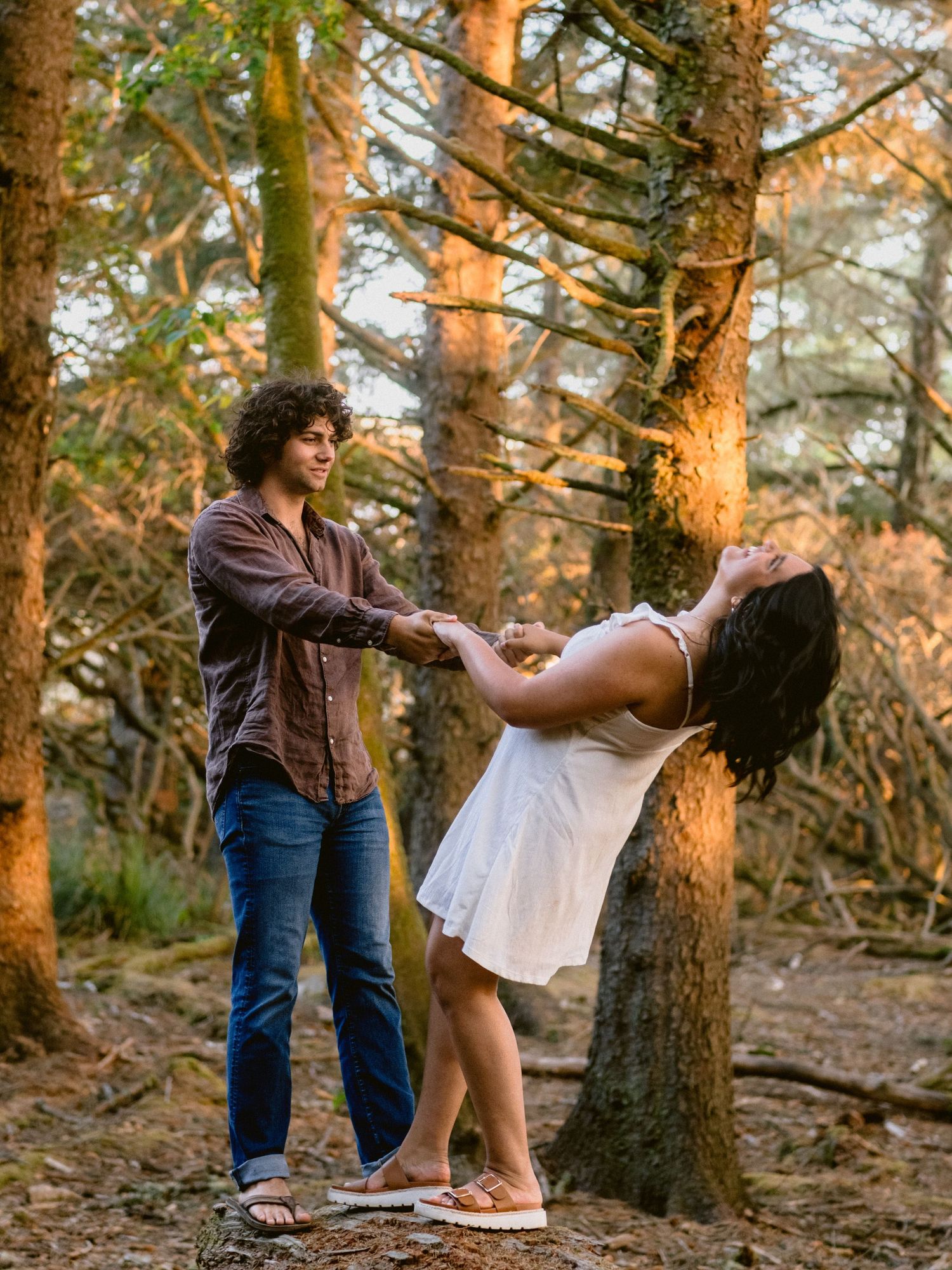 A couple shares a romantic dance among sunlit trees in a forest.