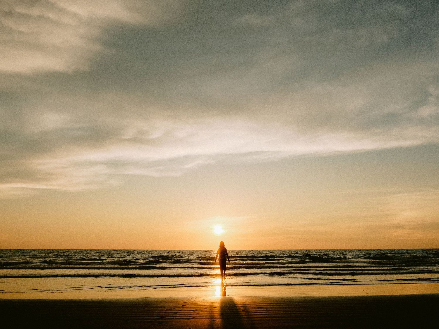 Minimalist beach sunset with silhouette figure walking along shoreline.