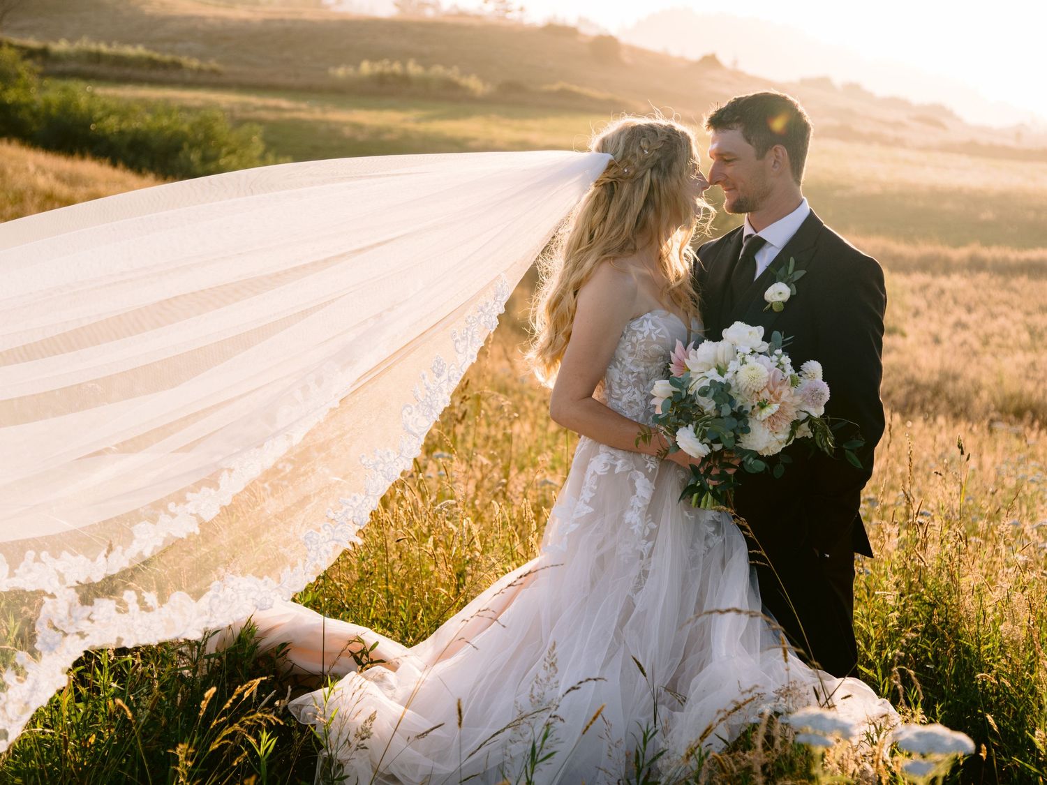 Bride and groom pose in golden sunset light in an open field.