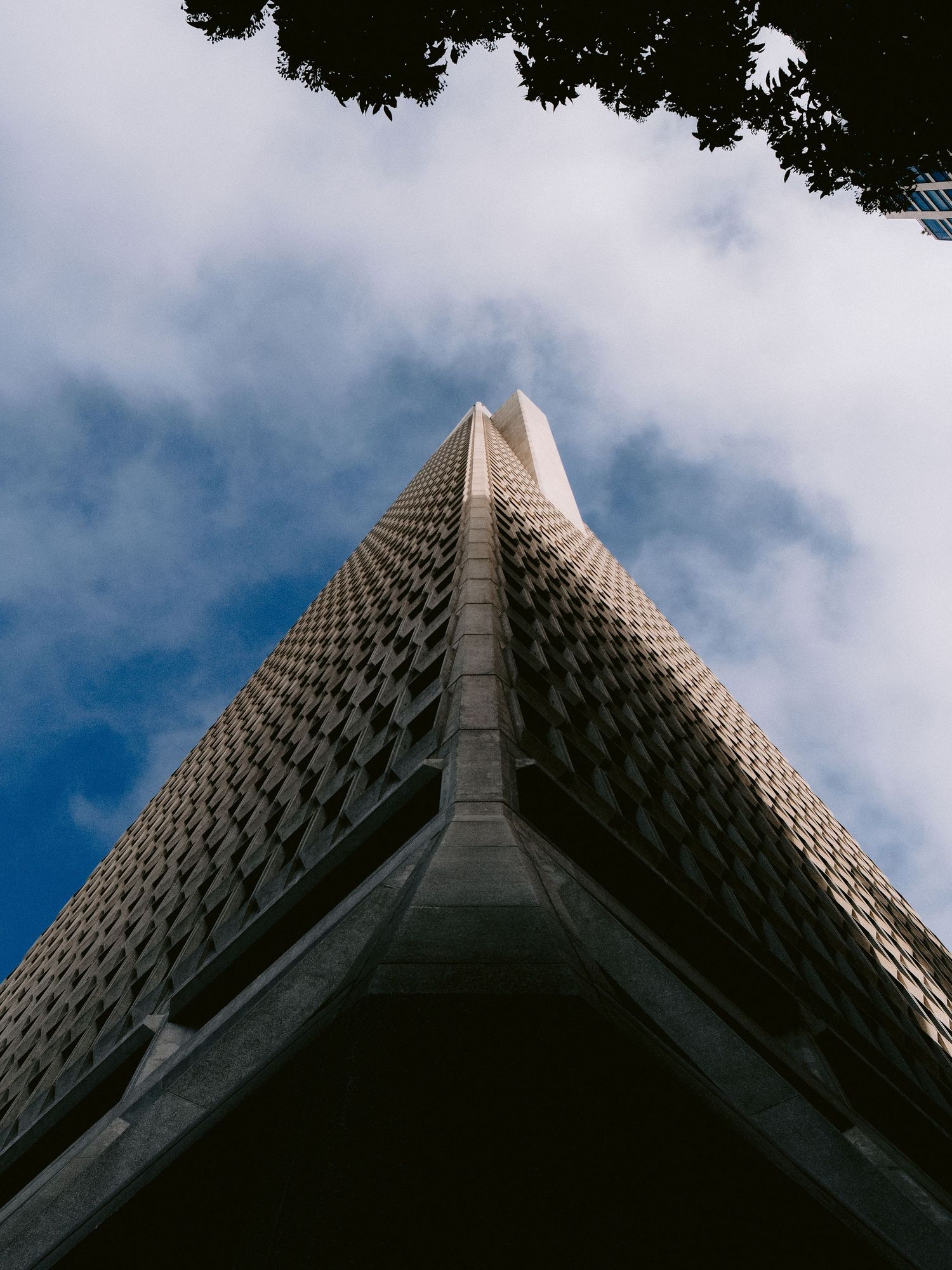 Upward architectural shots of a modern geometric building facade against blue sky and clouds.