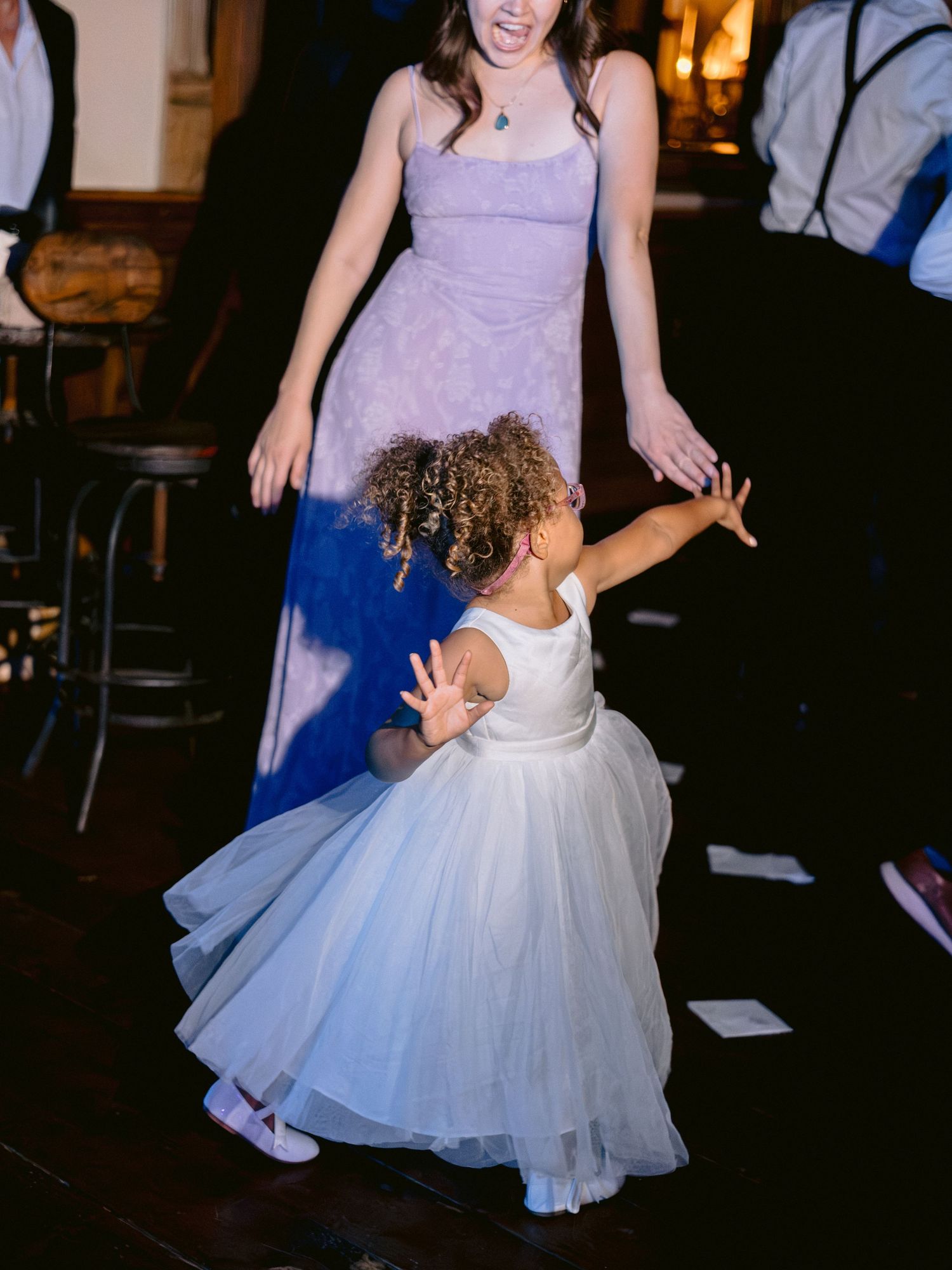 A flower girl in a white tulle dress twirls on the dance floor during a wedding reception.