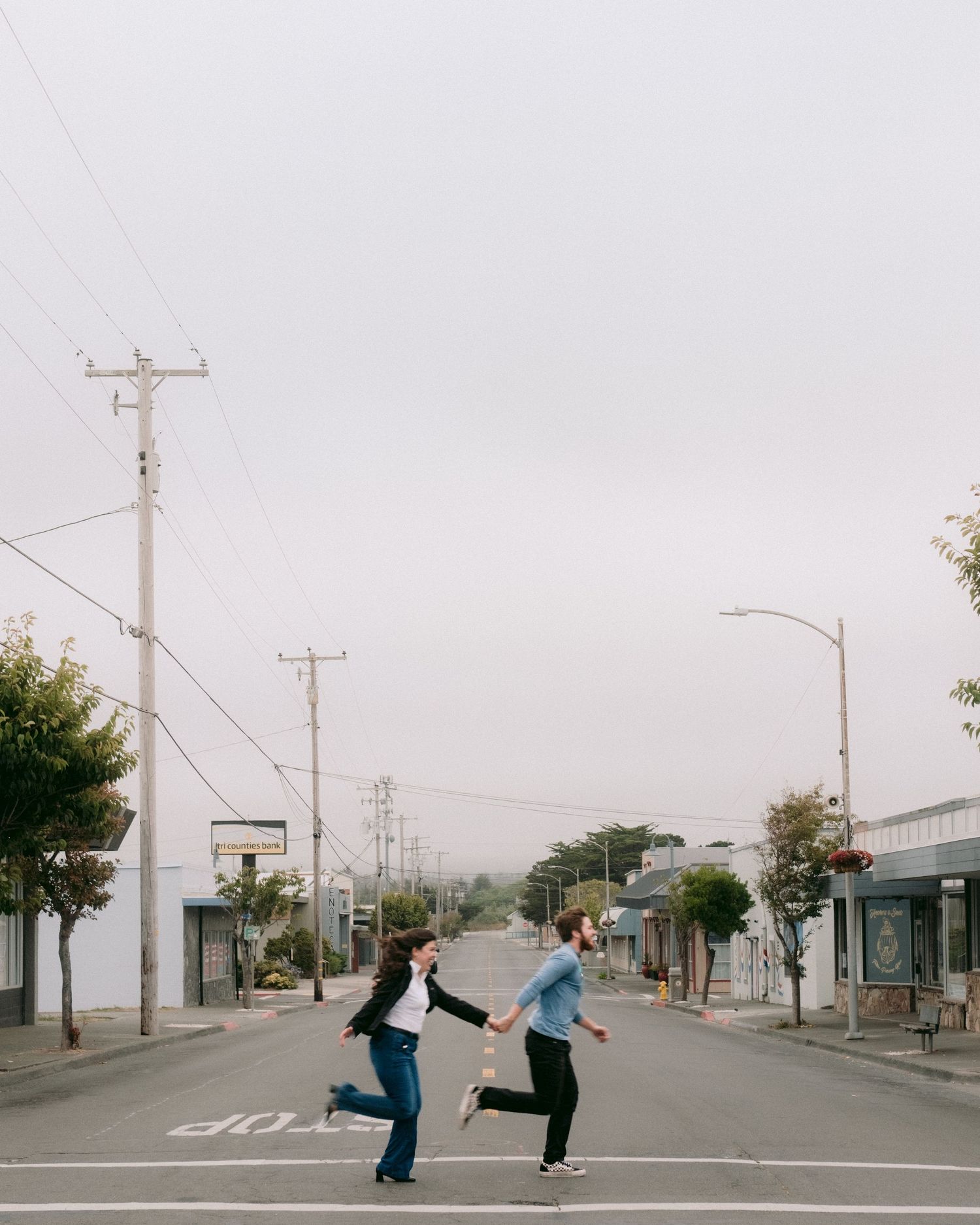 A couple dances playfully in an empty street with utility poles and foggy sky.
