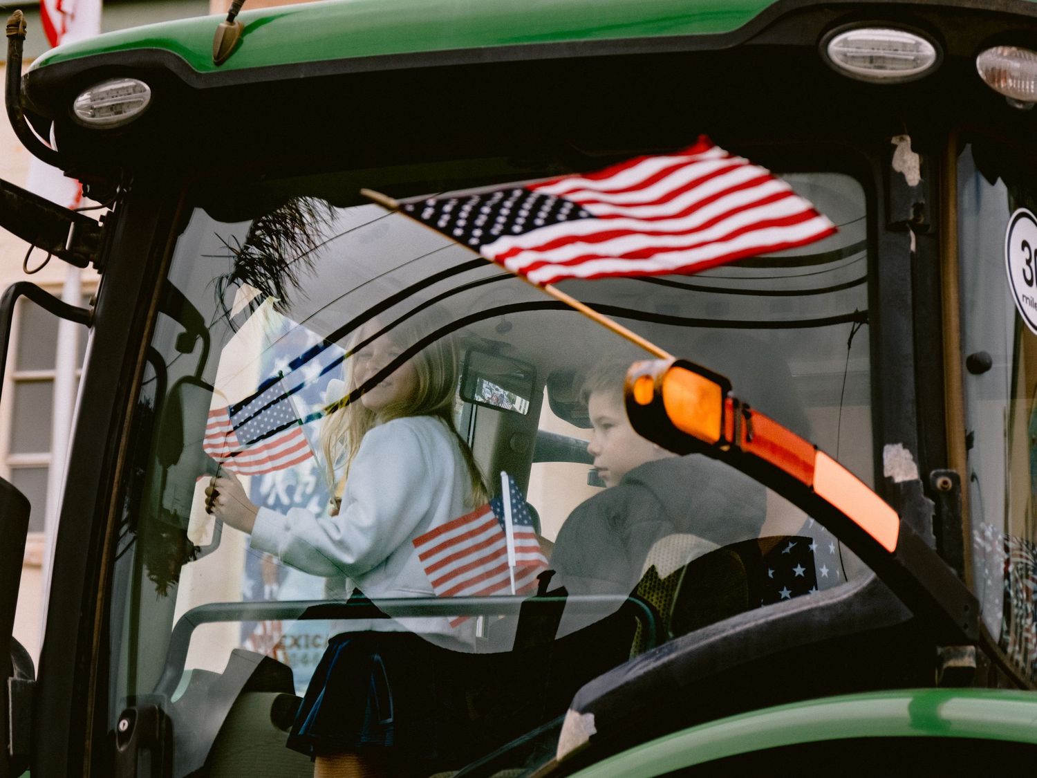 American flags mounted on green tractor cab during patriotic display.