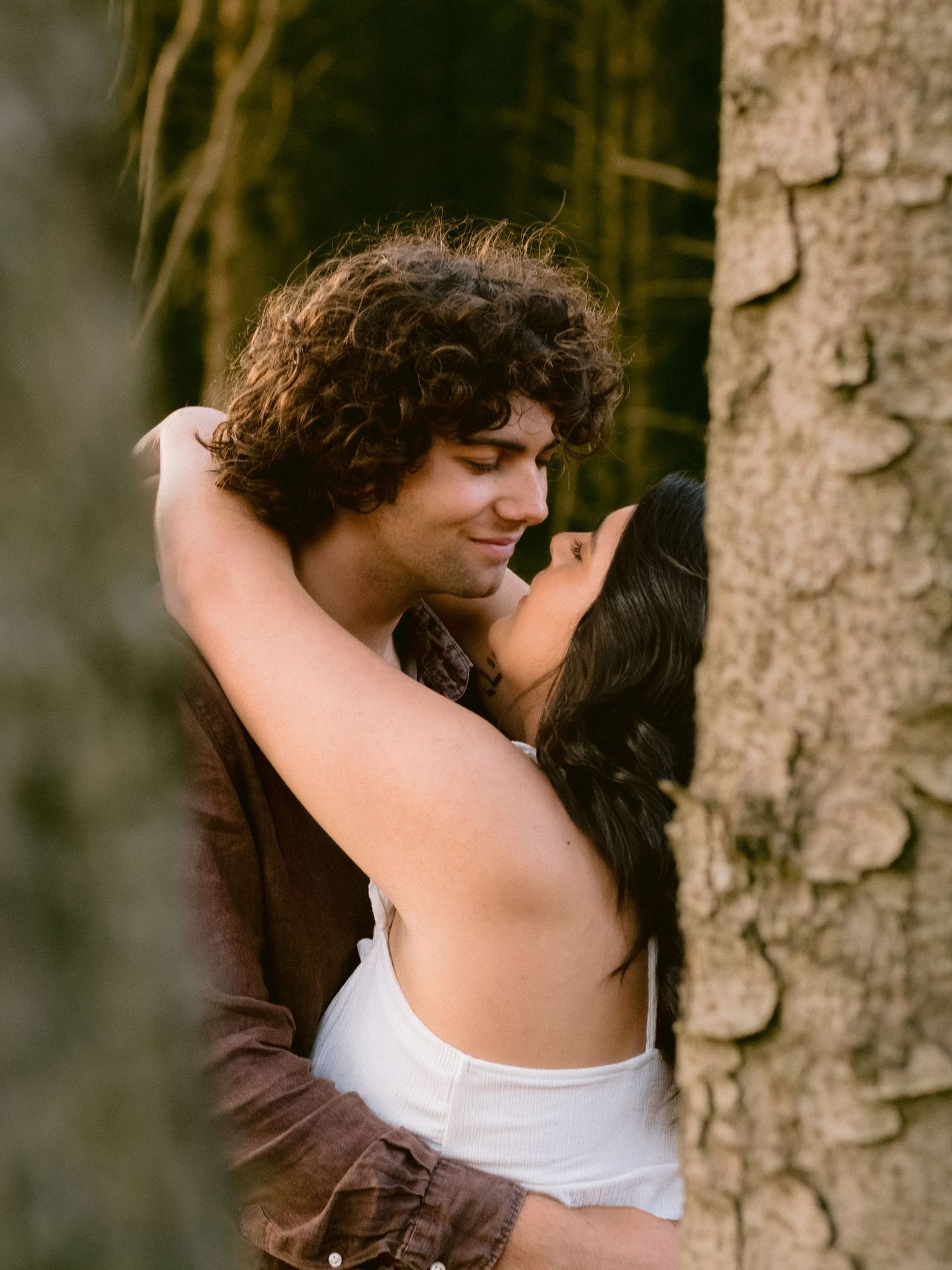 A tender embrace captured in close-up against a tree trunk background.