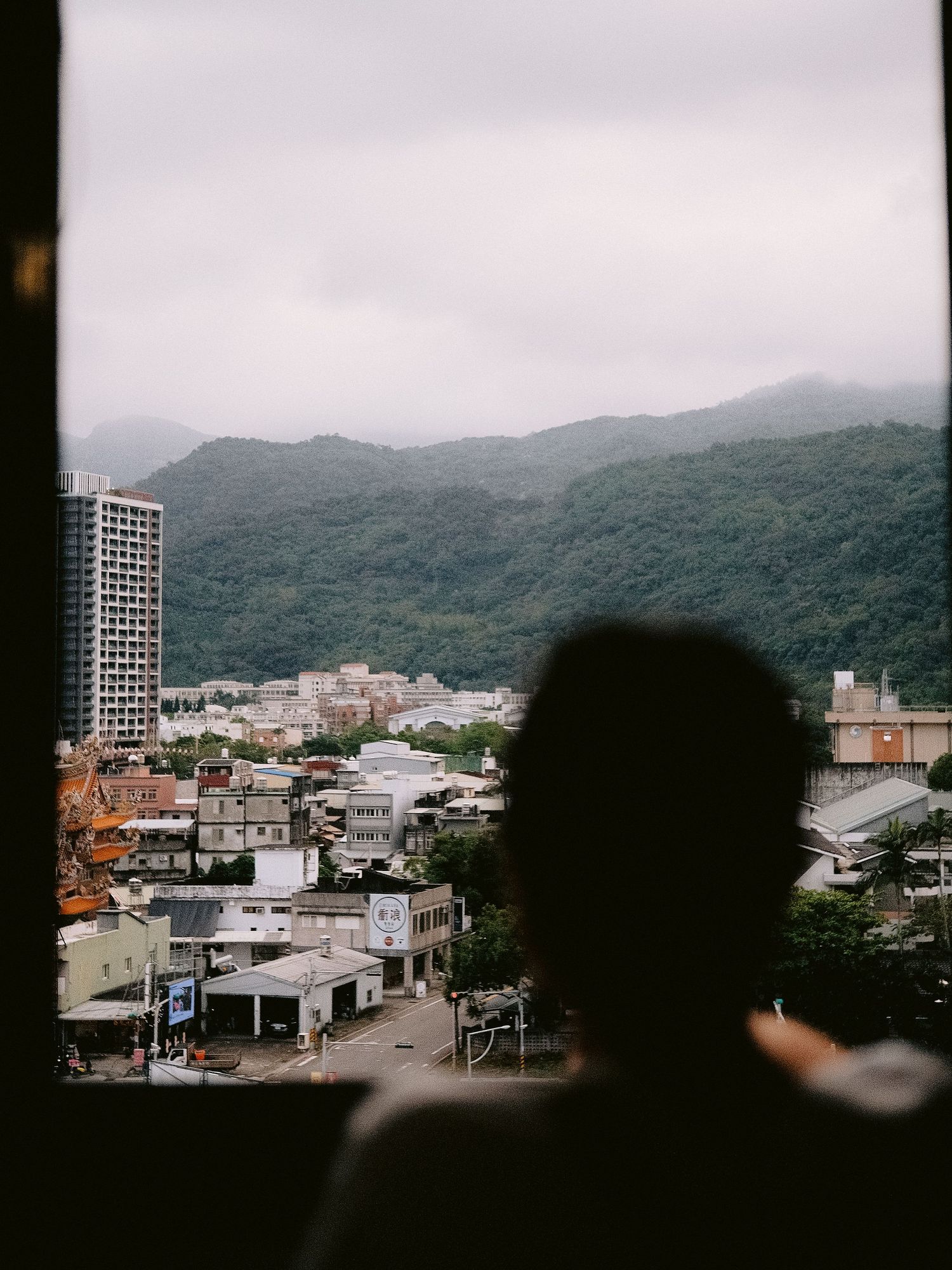Aerial view of a misty mountainous cityscape with buildings nestled among green hills.