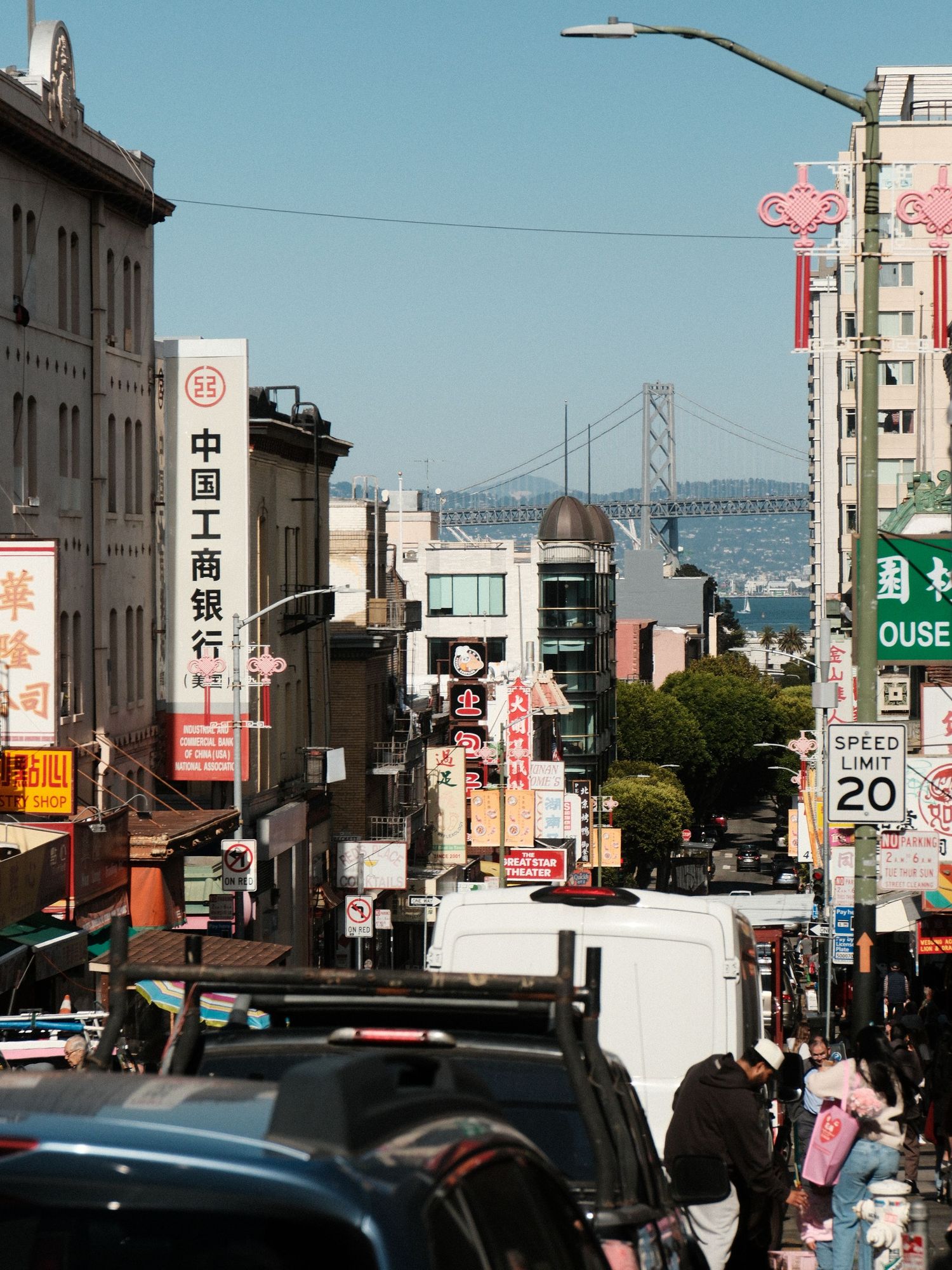 View down a San Francisco Chinatown street with the Bay Bridge visible in the distance.