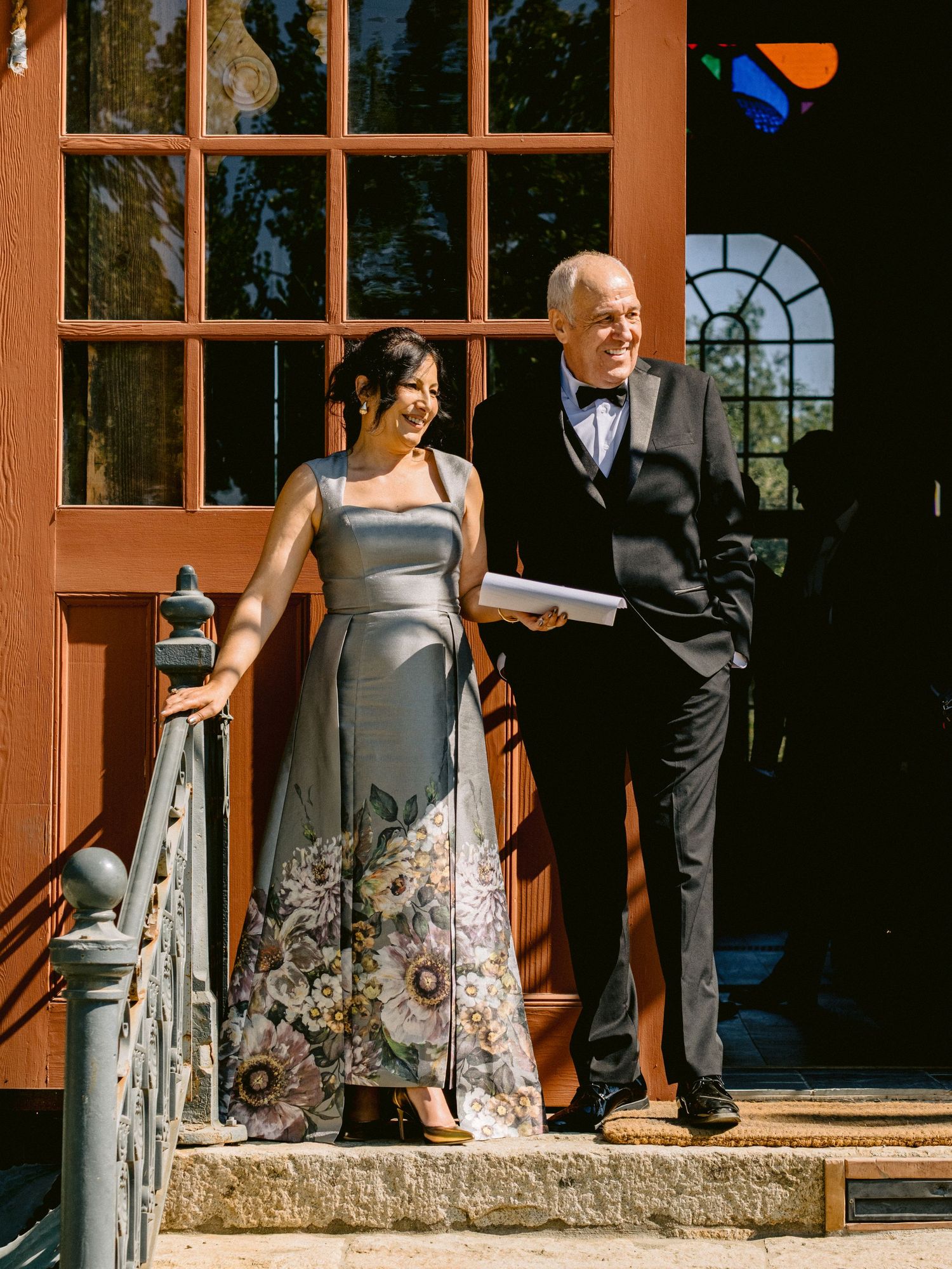 Wedding party members in formal attire stand along a rustic wooden porch.