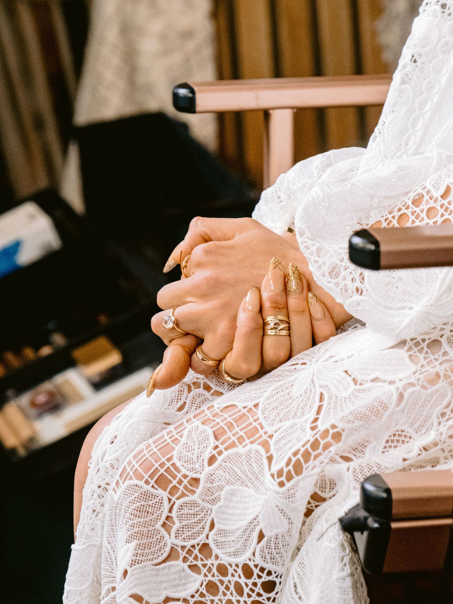 Close-up of lace wedding dress detail with hands showing wedding rings.