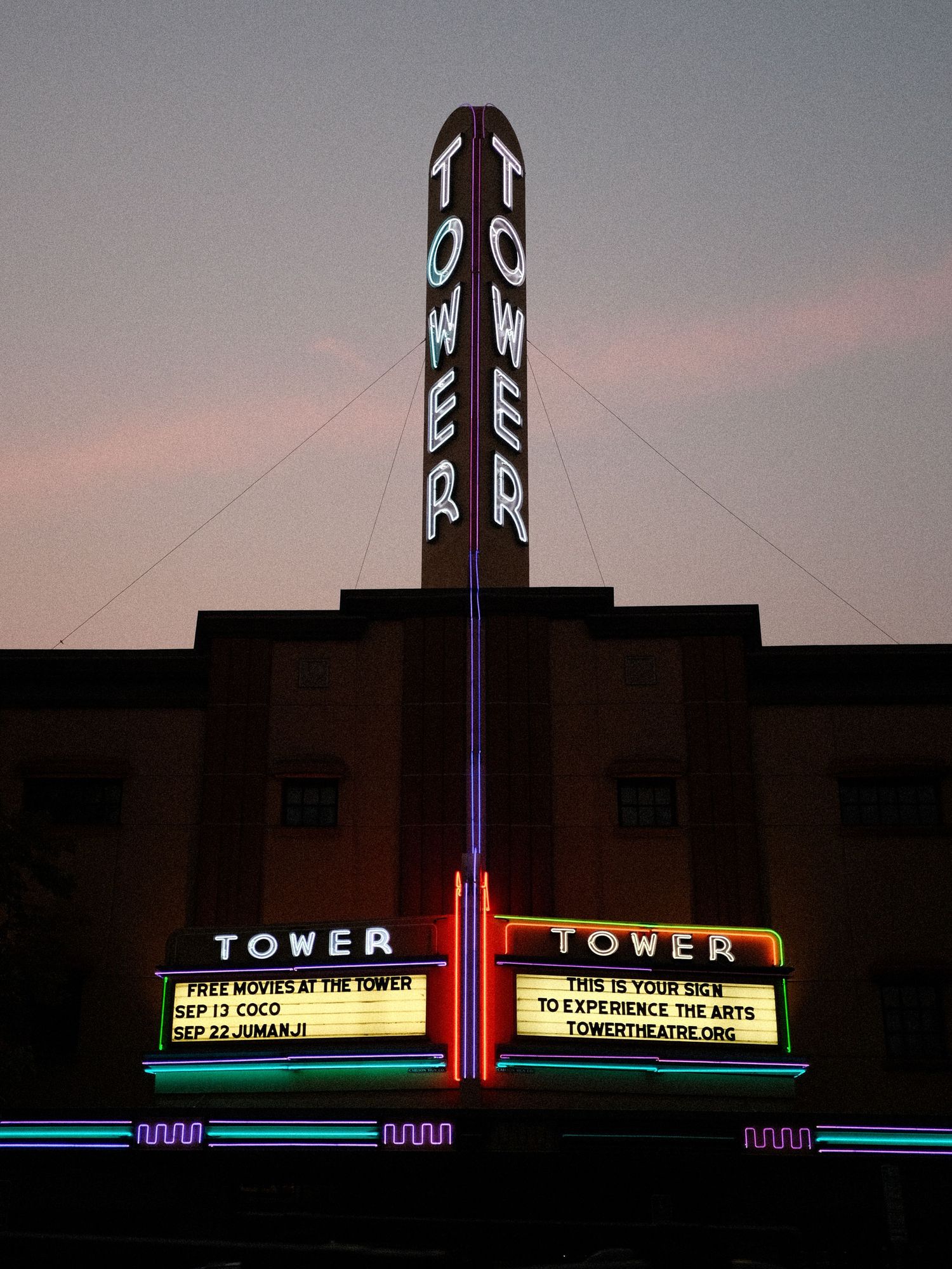 Art deco Tower Theater facade illuminated at dusk with movie titles on marquee.