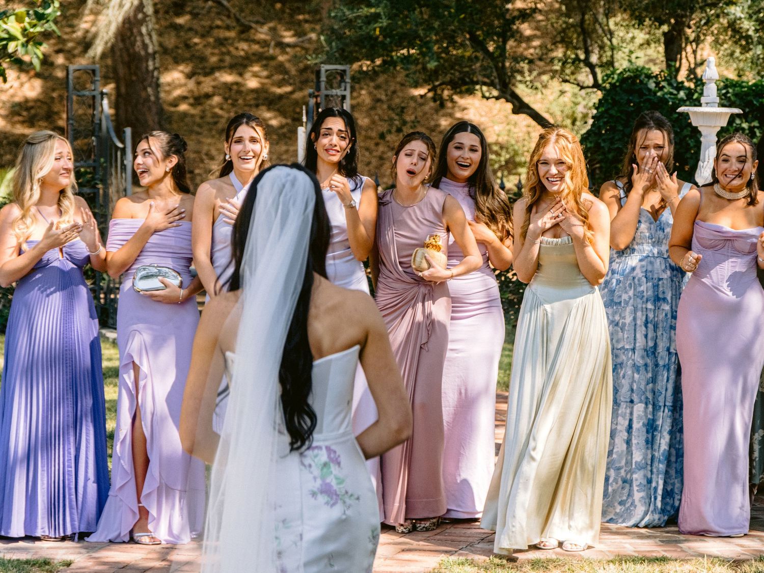 Bridesmaids in lavender dresses pose together outdoors for a wedding photo.