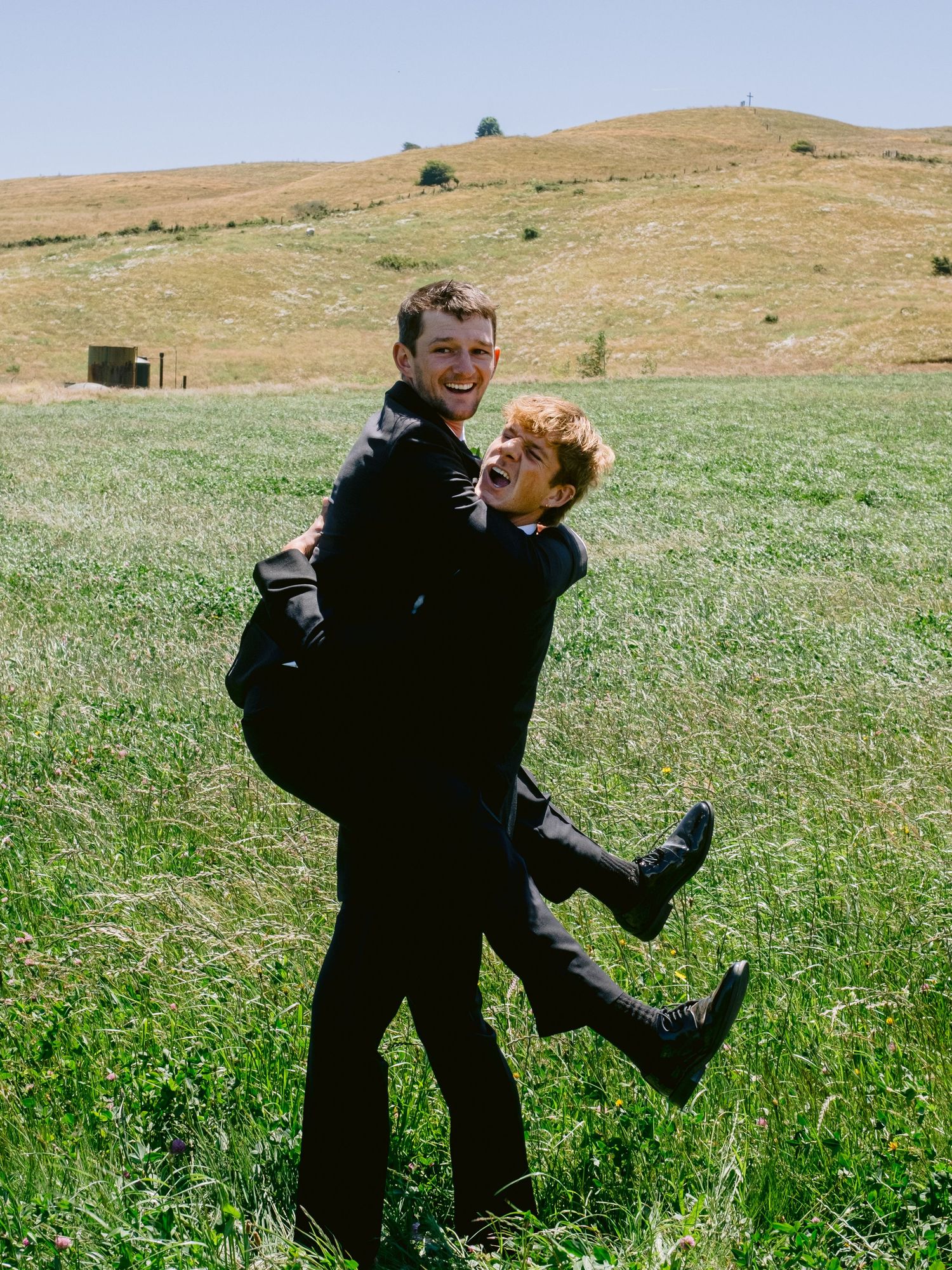 Playful couple in formal attire enjoying moments together in a sunny meadow.