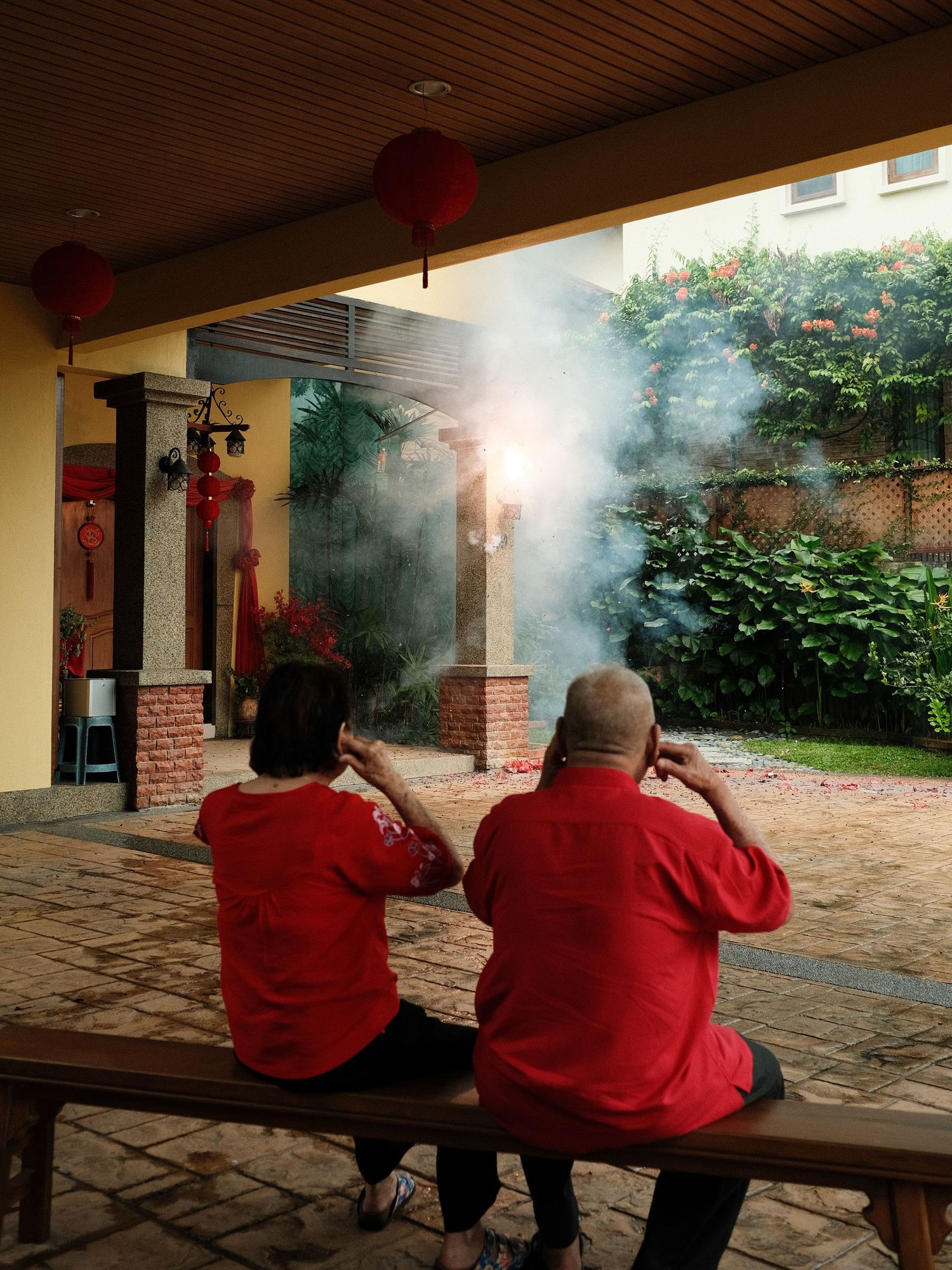 Two people in red shirts sitting on a bench shooting at a target range.
