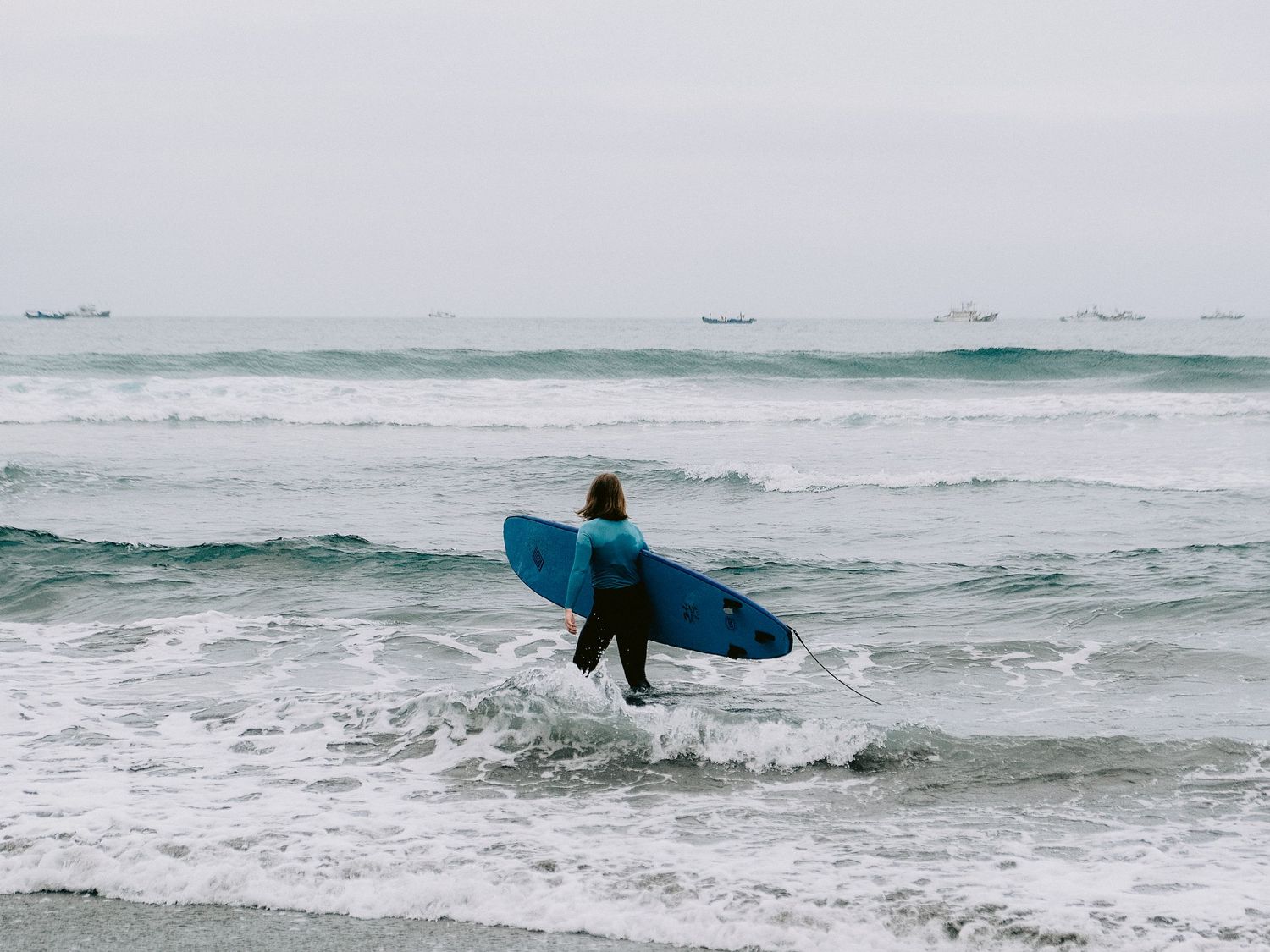 Surfer walking along a misty beach with crashing waves.