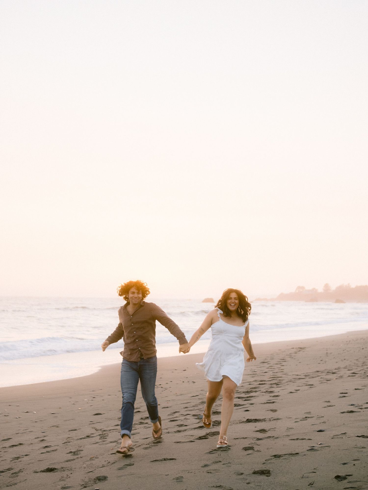 Couple running and playing together on a sandy beach at sunset.