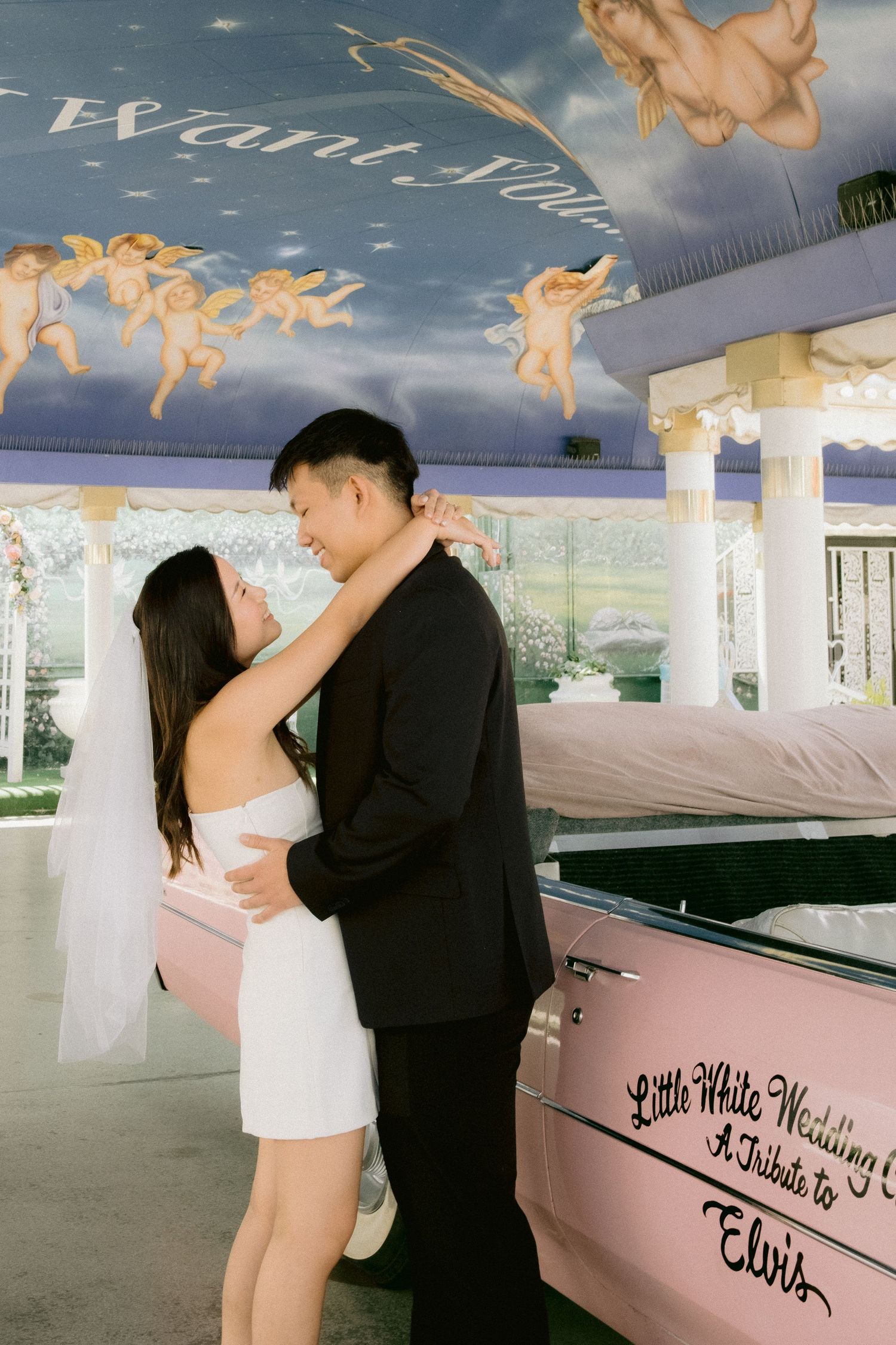 A couple shares intimate moments inside a pink and white decorated wedding chapel.