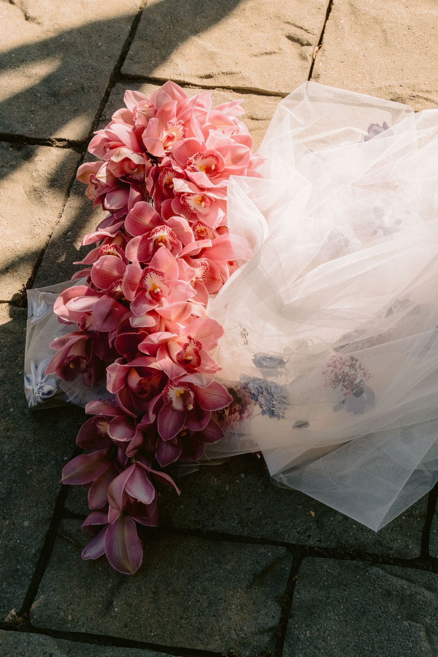 Pink orchid bouquet draped over white tulle fabric on stone surface.