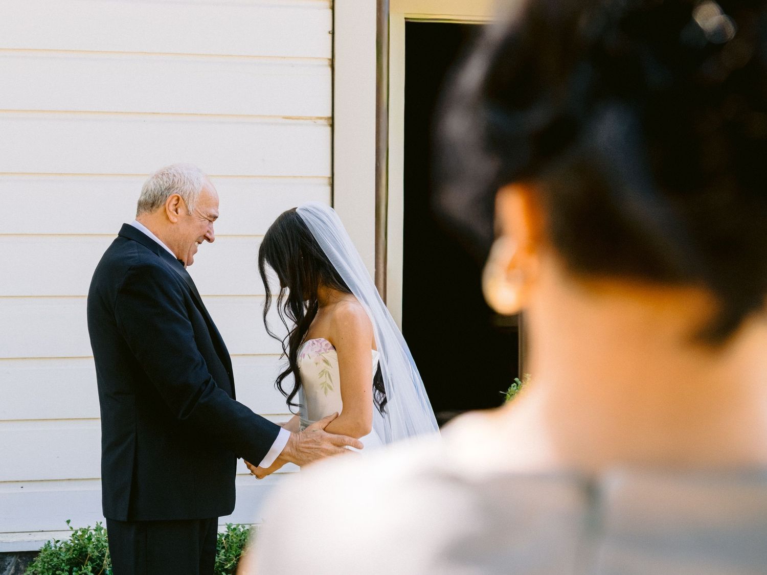 Wedding ceremony taking place outside a white building on a sunny day.
