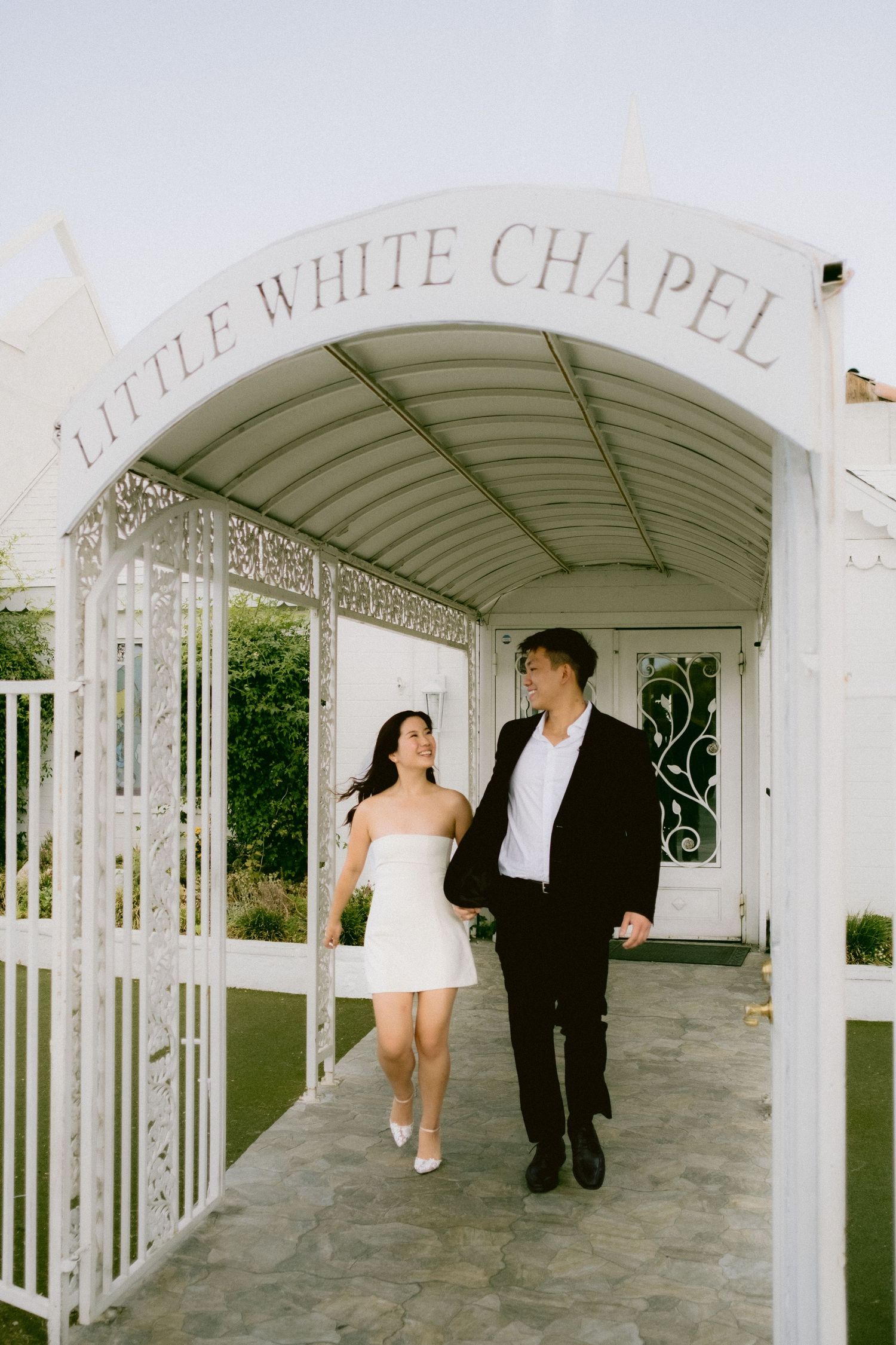 Newlyweds walking through the white arched corridor of a Las Vegas wedding chapel.